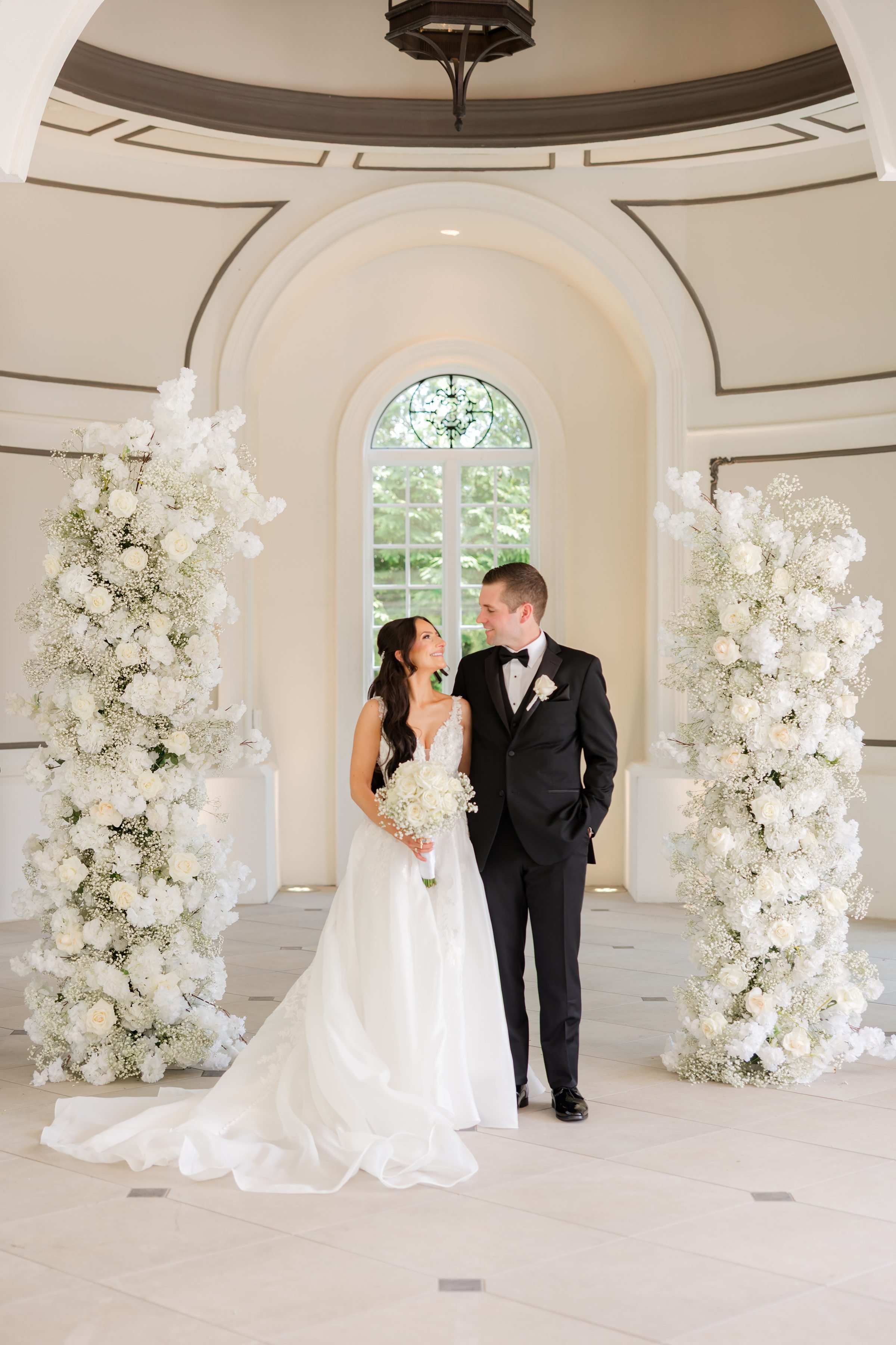 Bride and groom by the wedding altar, smiling at each other with flowers to the side