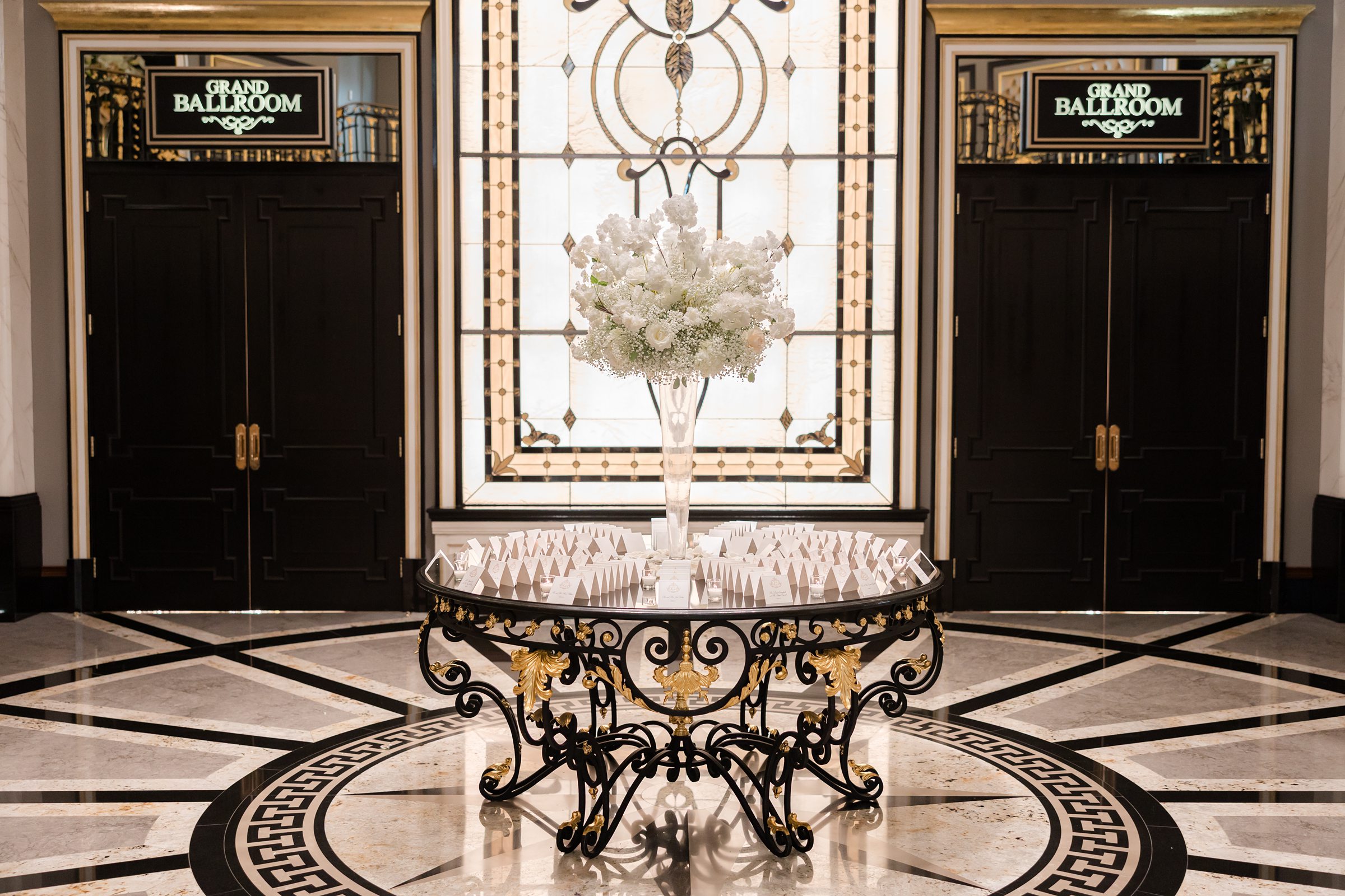 Shadowbrook entryway with gold and black palette, large flower setup in the center surrounded by table/welcome cards