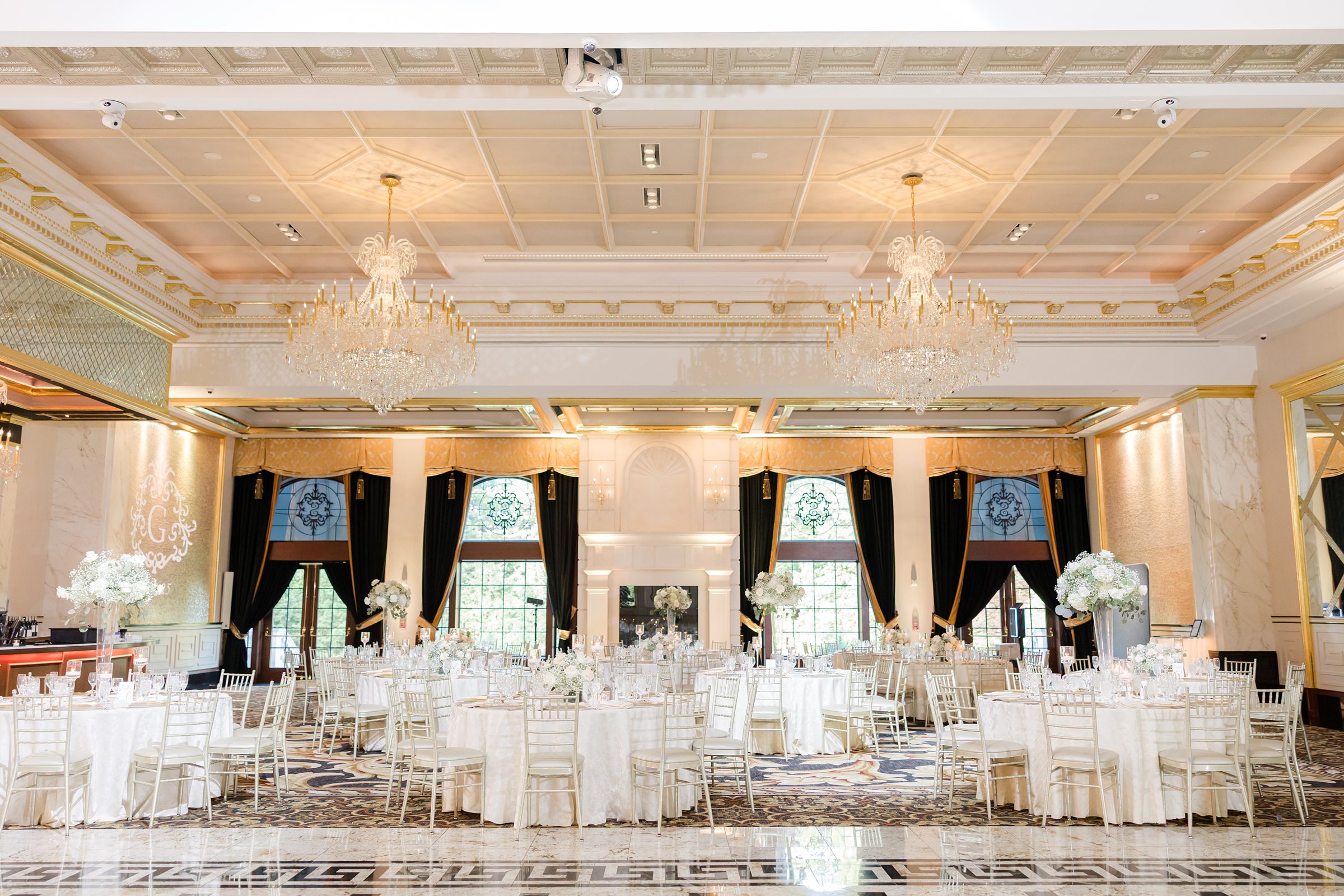 An empty wedding reception hall decorated with white classic white roses with white table curtain, with warm chandelier at the top