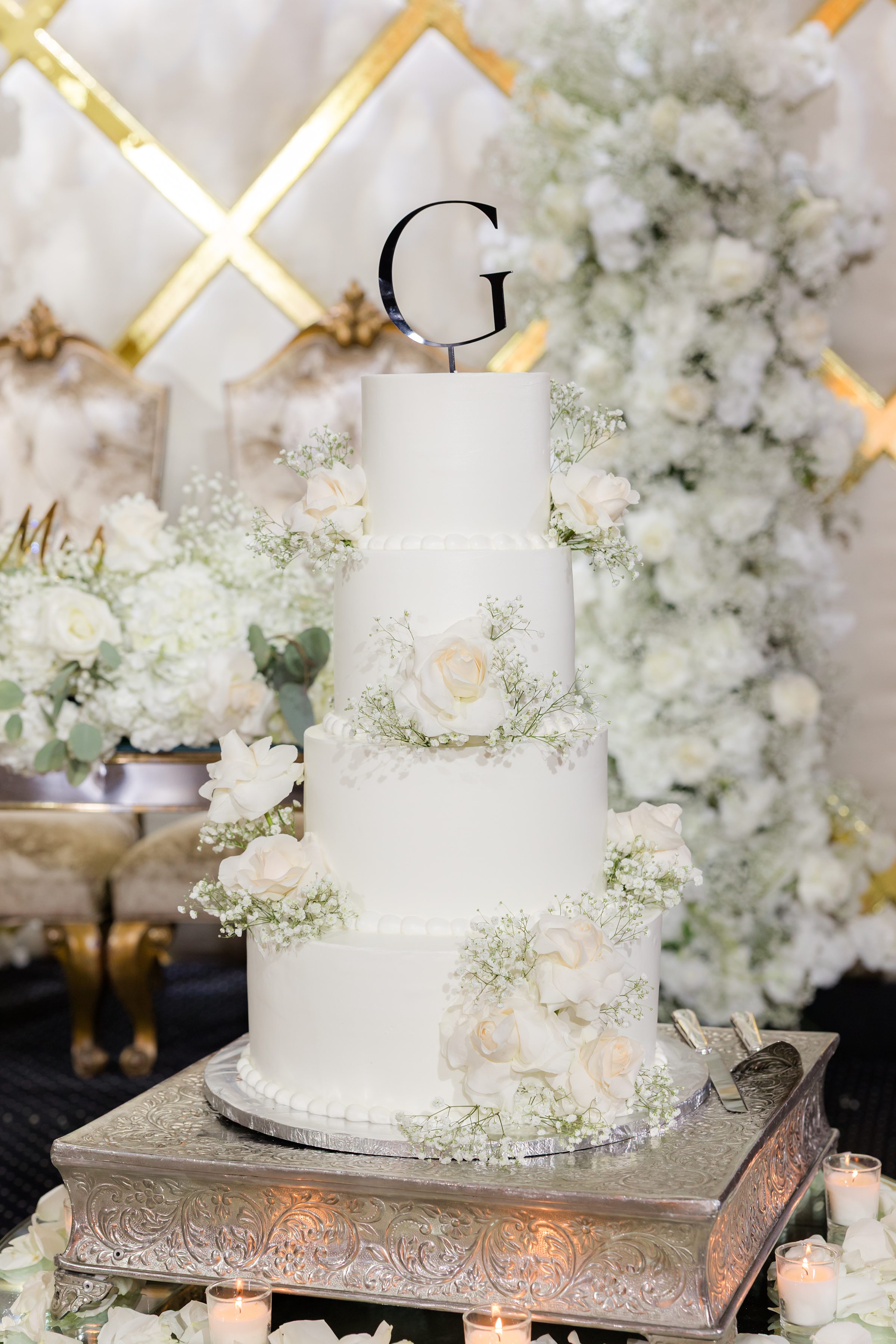 a shot of 4-layered white wedding cake with letter G initial
