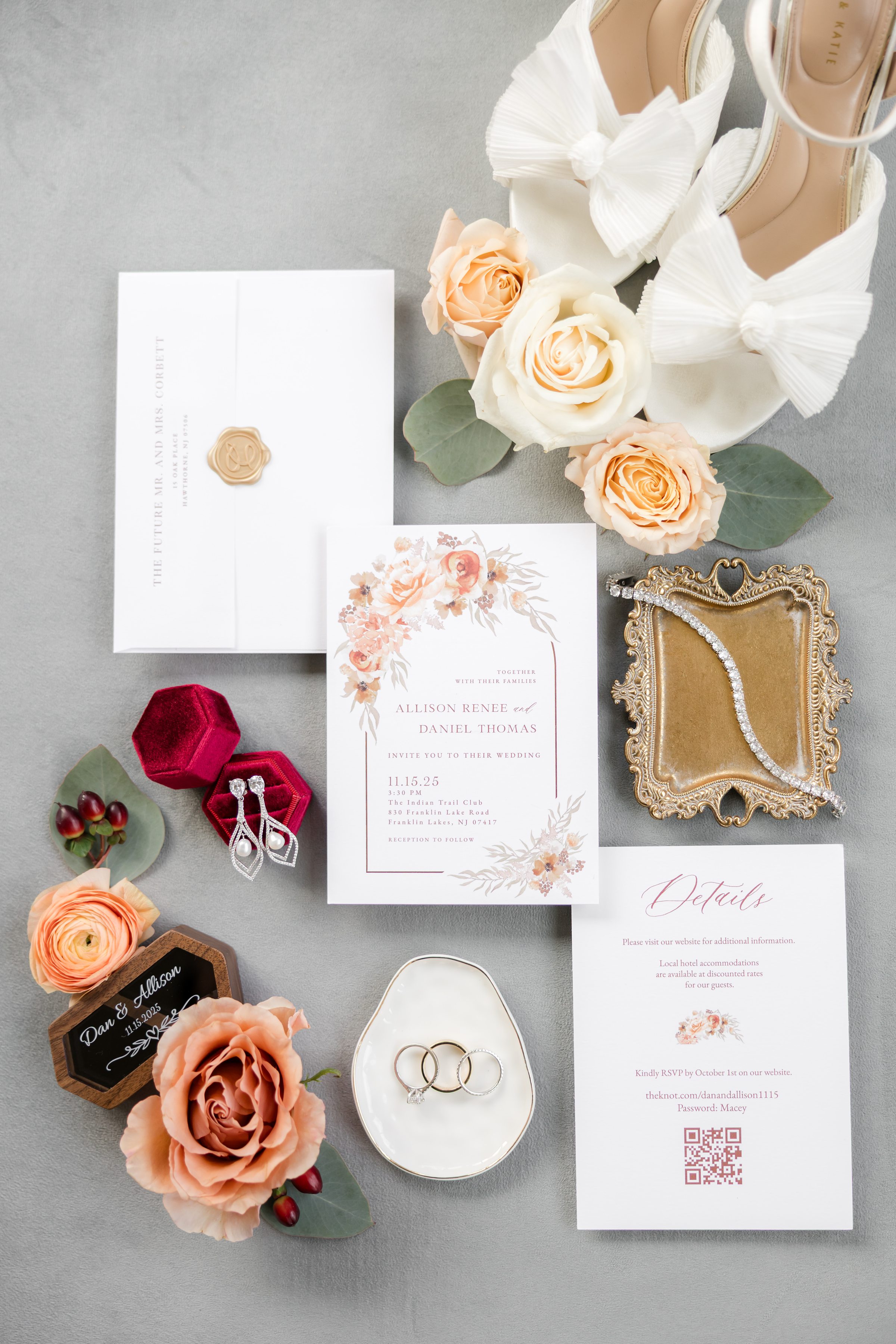 Wedding invitation suite with floral accents, rings, jewelry, perfume, and styling details arranged on a gray background