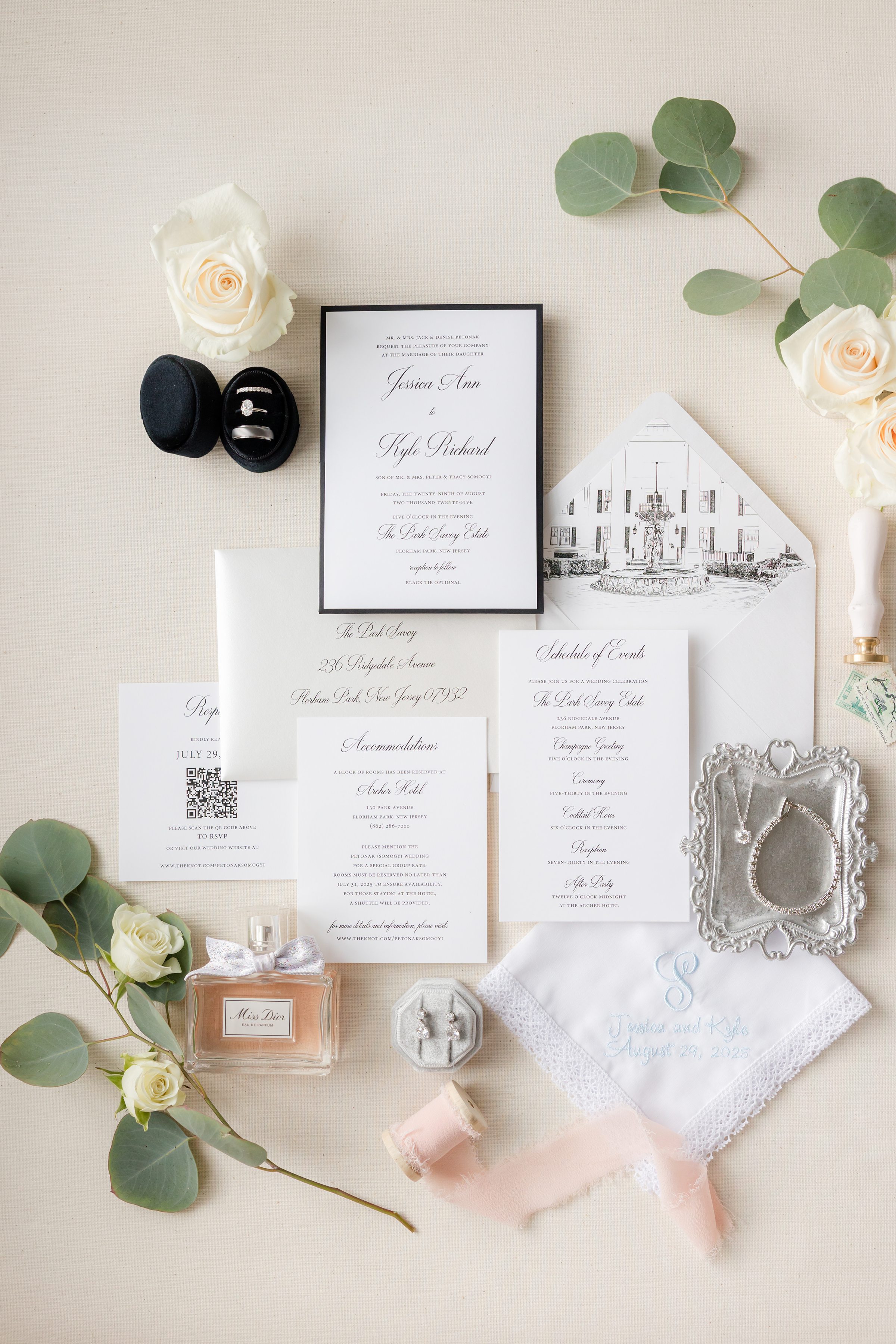 Detail shot of wedding invite, and bridal items, including silver jewelry and peach-colored perfume, with white rose and leaves as accents
