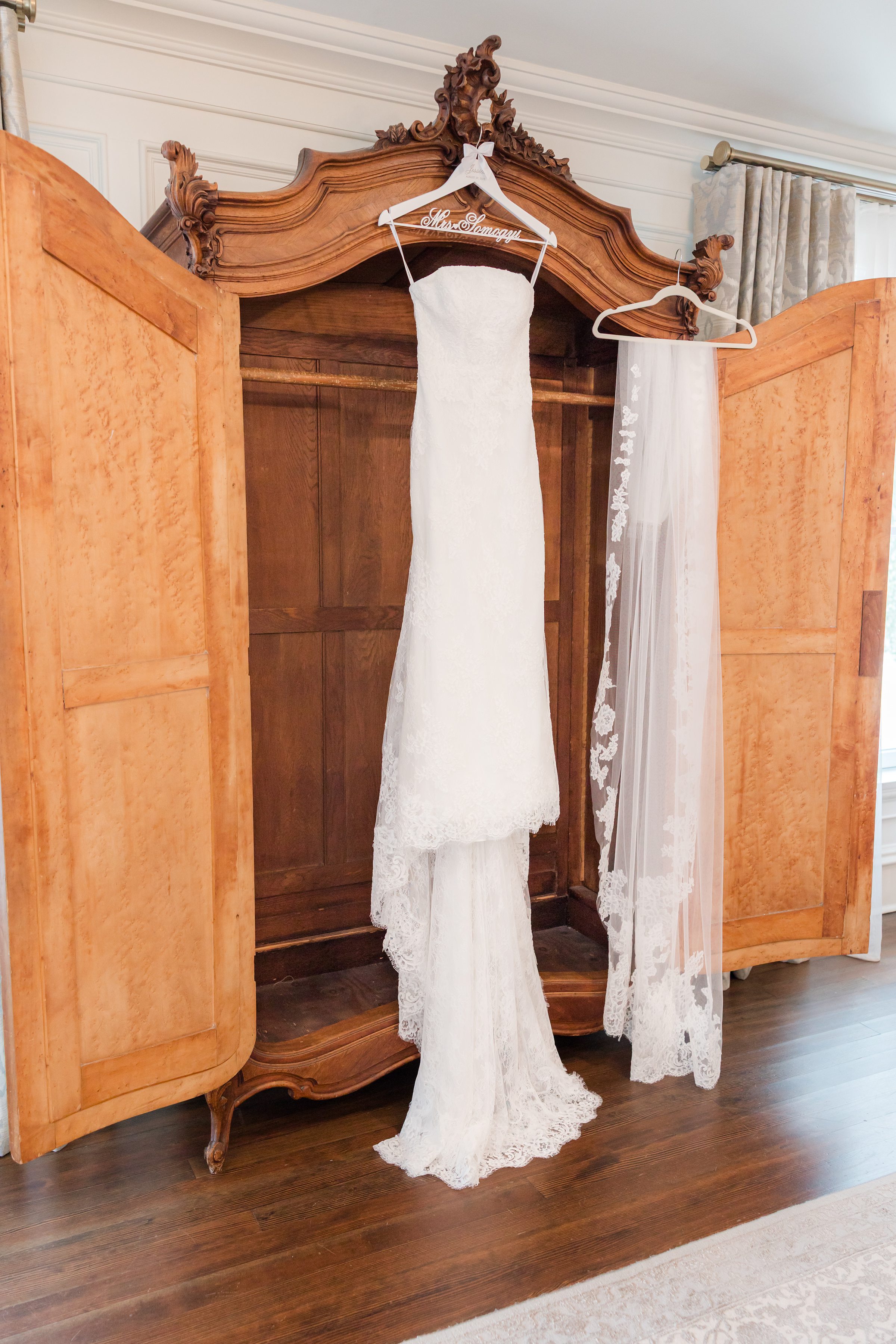 Wedding dress hung on top of an open wooden wardrobe, together with a long, lace veil