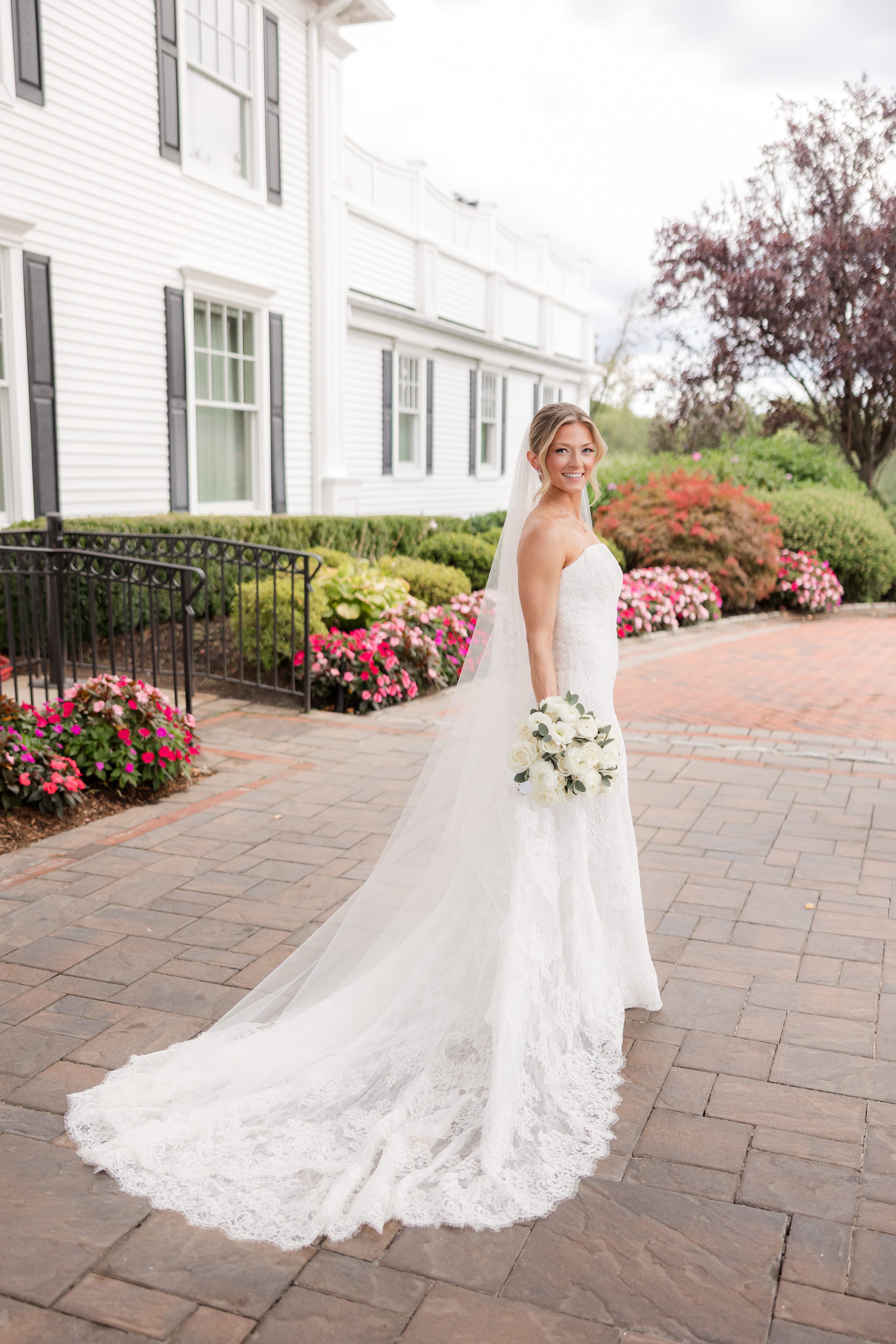 Bride posing at the entrance of Park Savoy Estate that is filled with pink flowers. Bride is looking back into the camera while holding her bouquet with her right hand