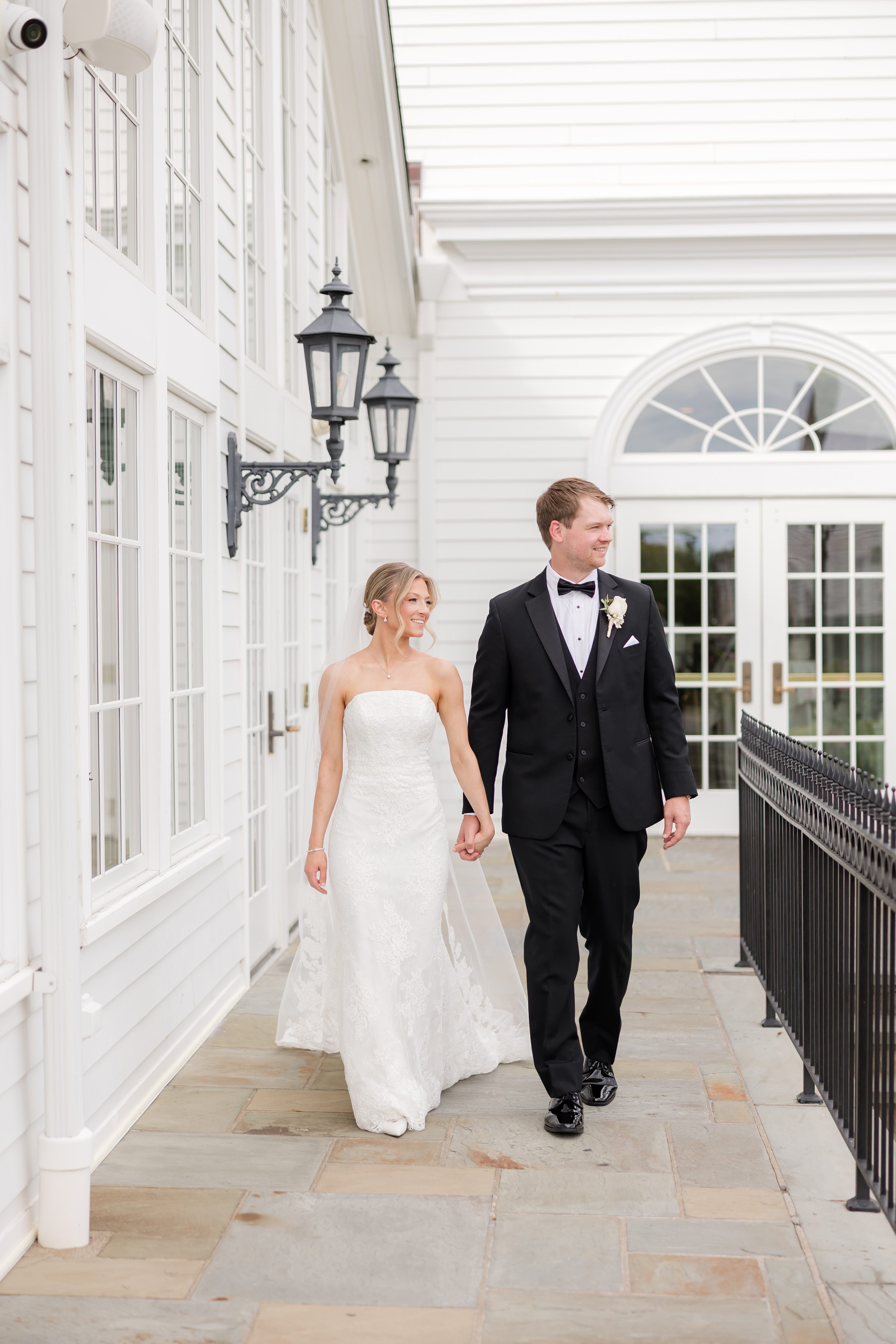 Bride and groom walking together hand-in-hand while looking to the right at the veranda