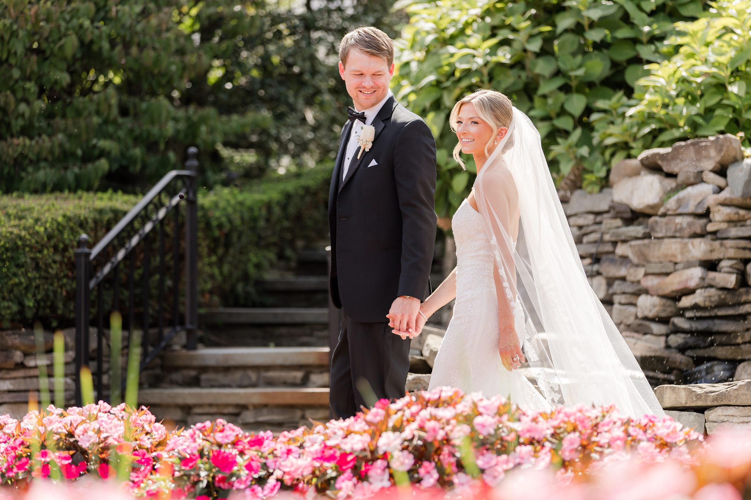 Landscape photo of the groom looking at the bride as they walk along the garden