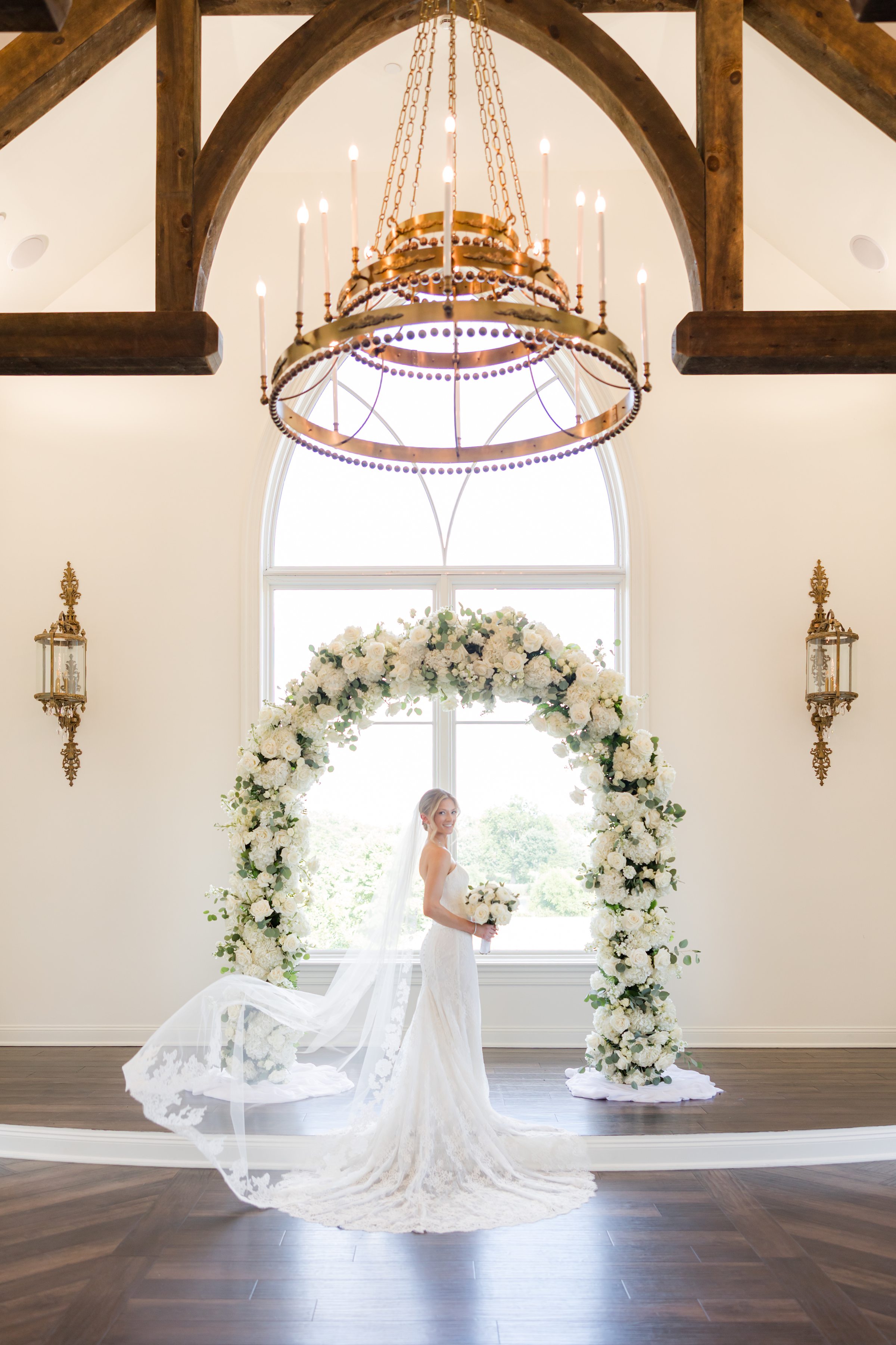Bride posing by the flower arch under the golden chandelier inside the chapel