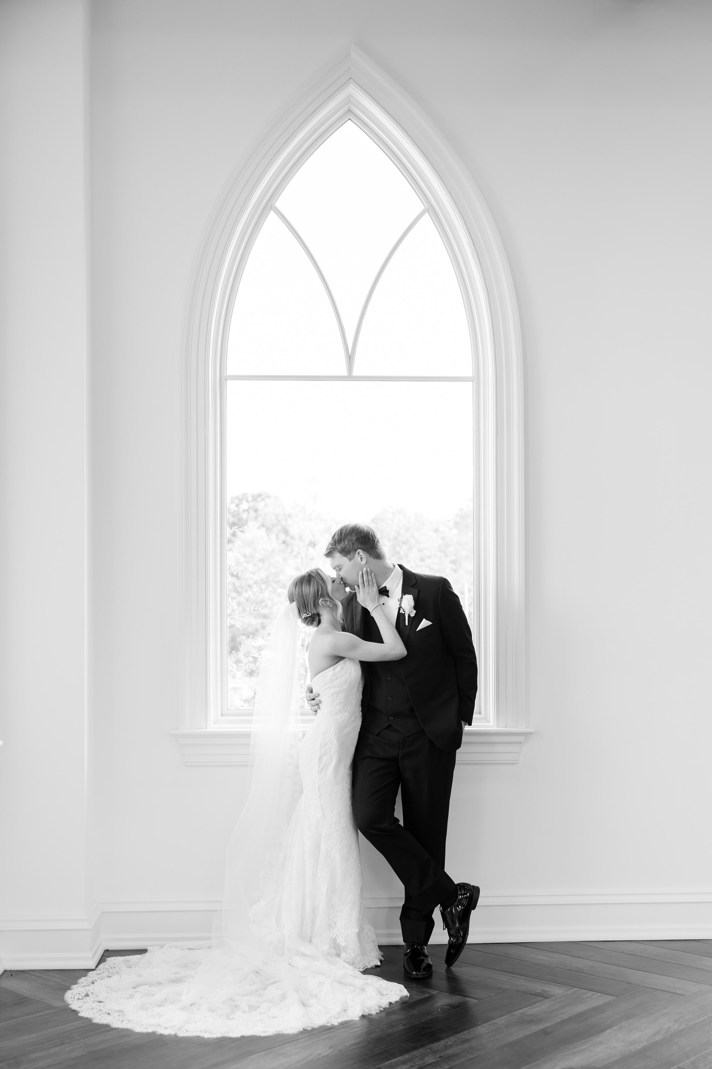 Black and white portrait of bride and groom kissing by the window