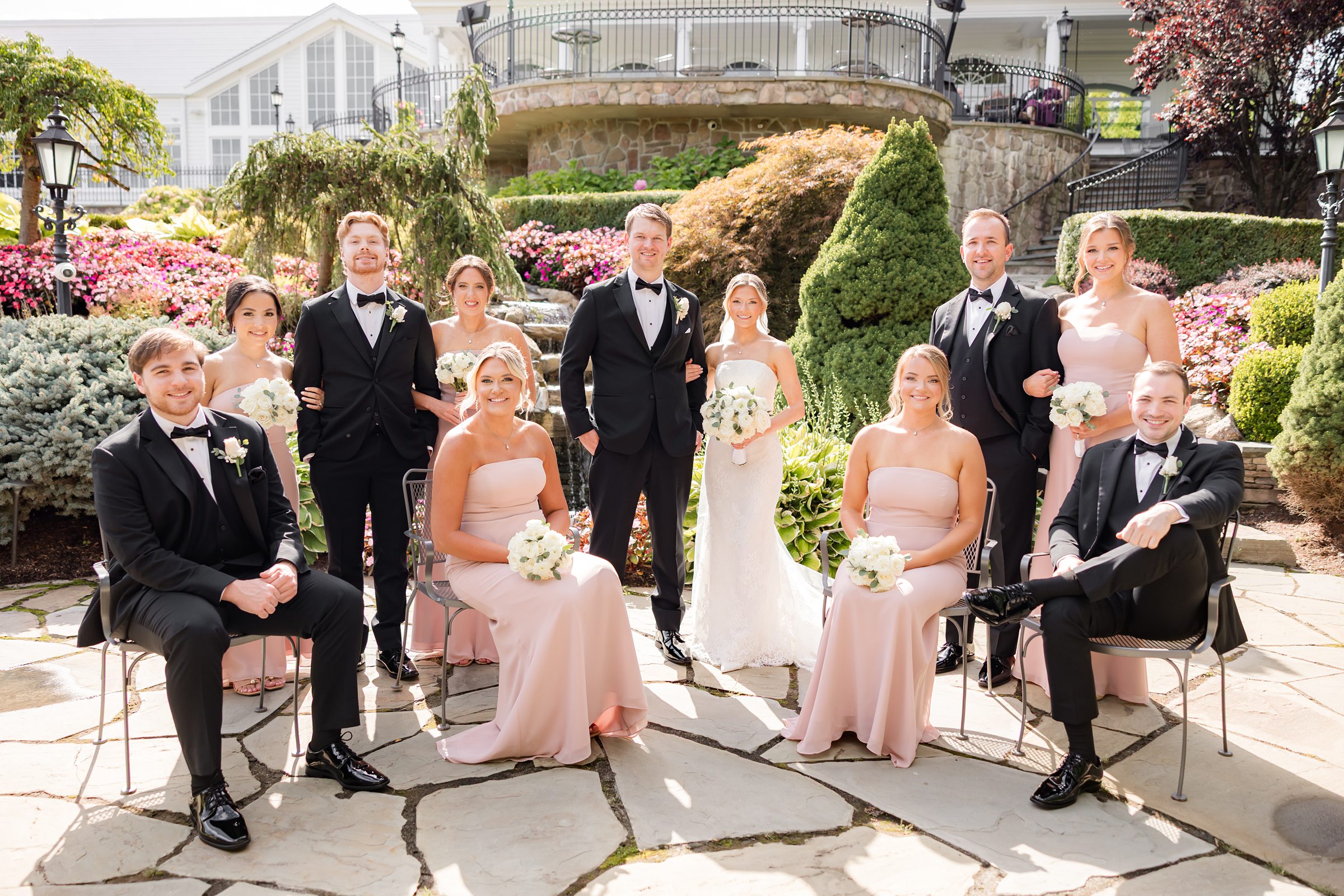 Bride and groom posed at the garden with the wedding party, some are seated, some are standing