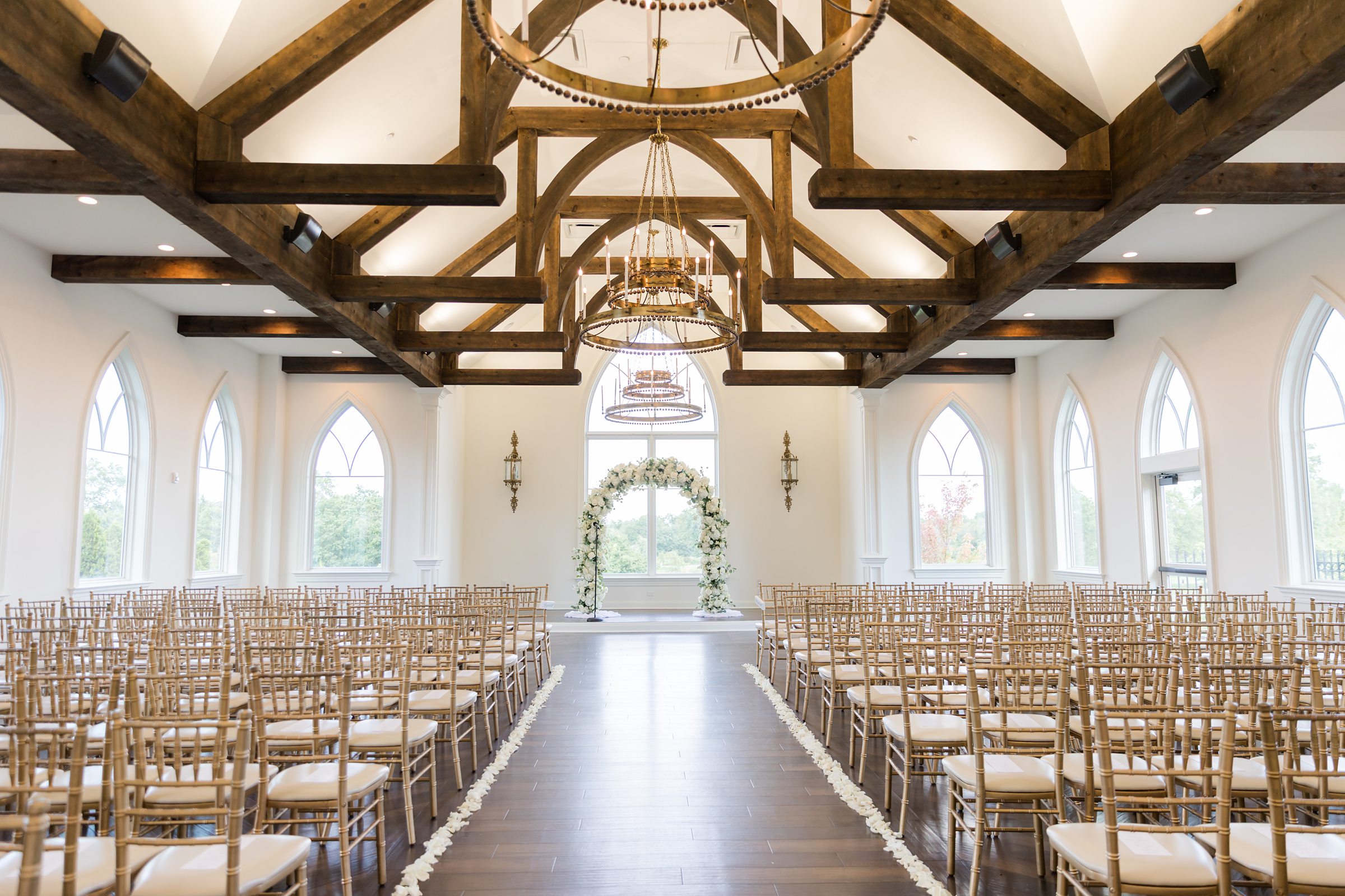 Photo of ceremony space with a white flower arch at the center, with wood accents