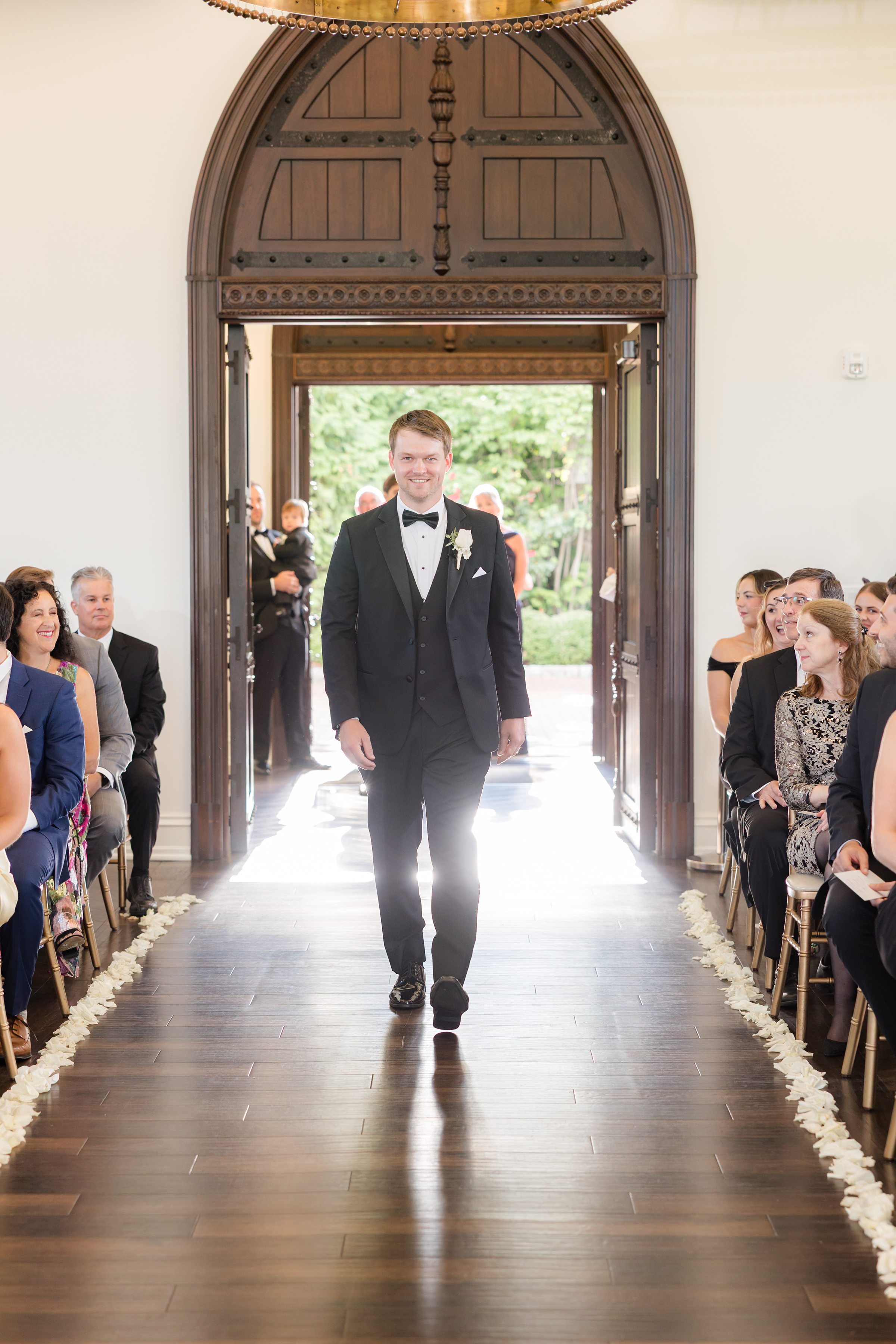 Photo of groom walking down the aisle while smiling, and a wooden doorway at the back