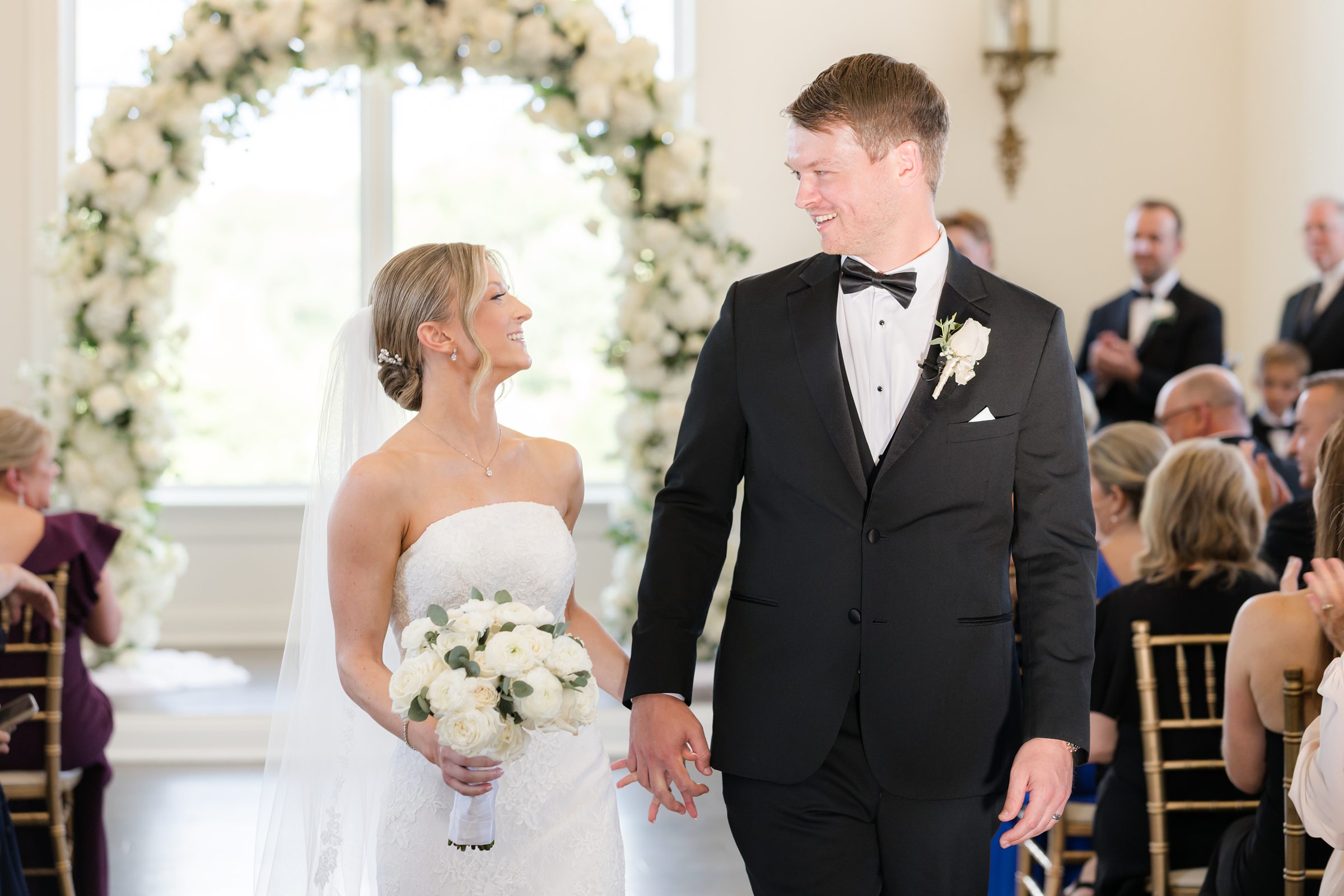 Landscape photo of bride and groom holding hands and looking at each other as they exit the aisle