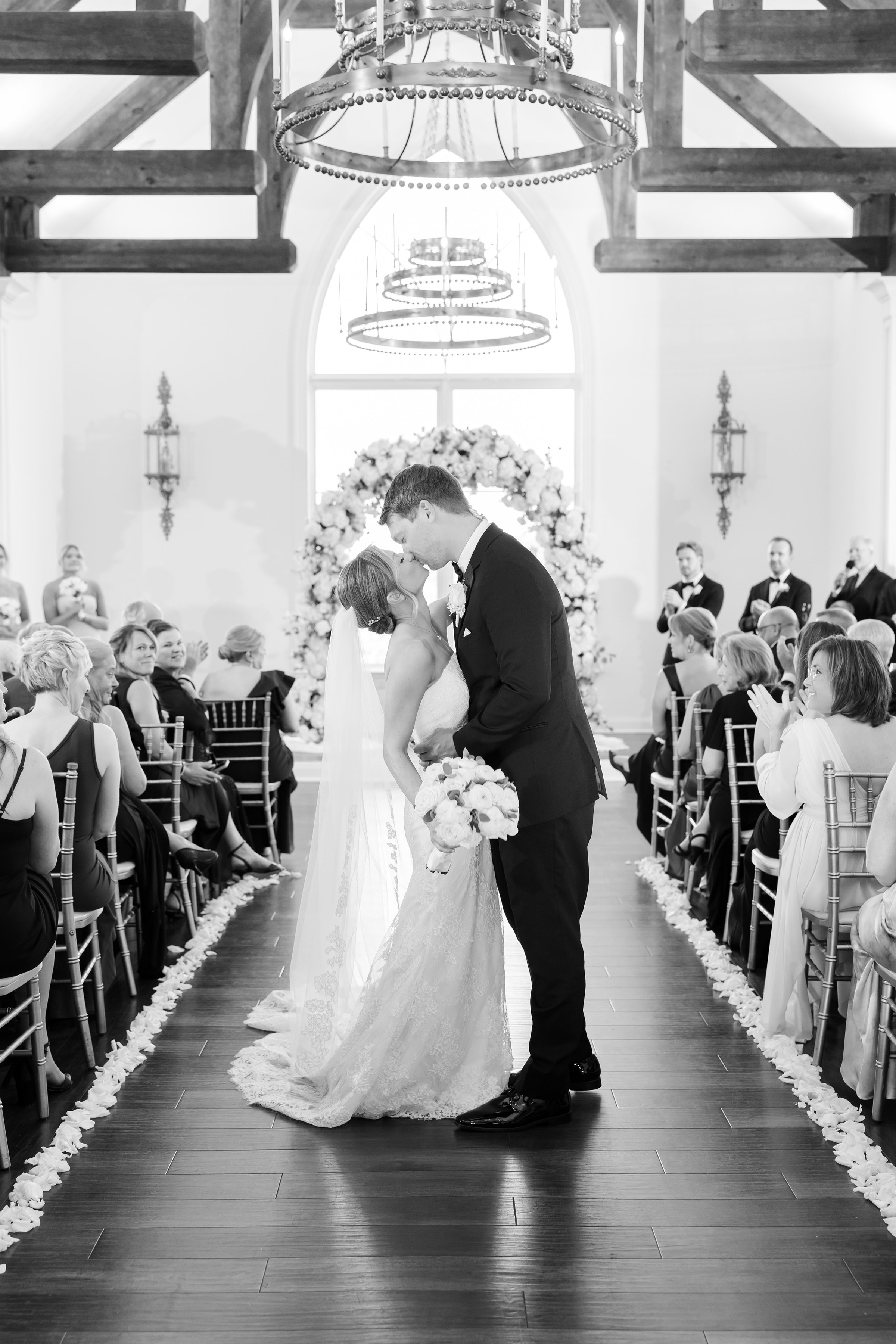 Black and white portrait of bride and groom kissing in the middle of the aisle
