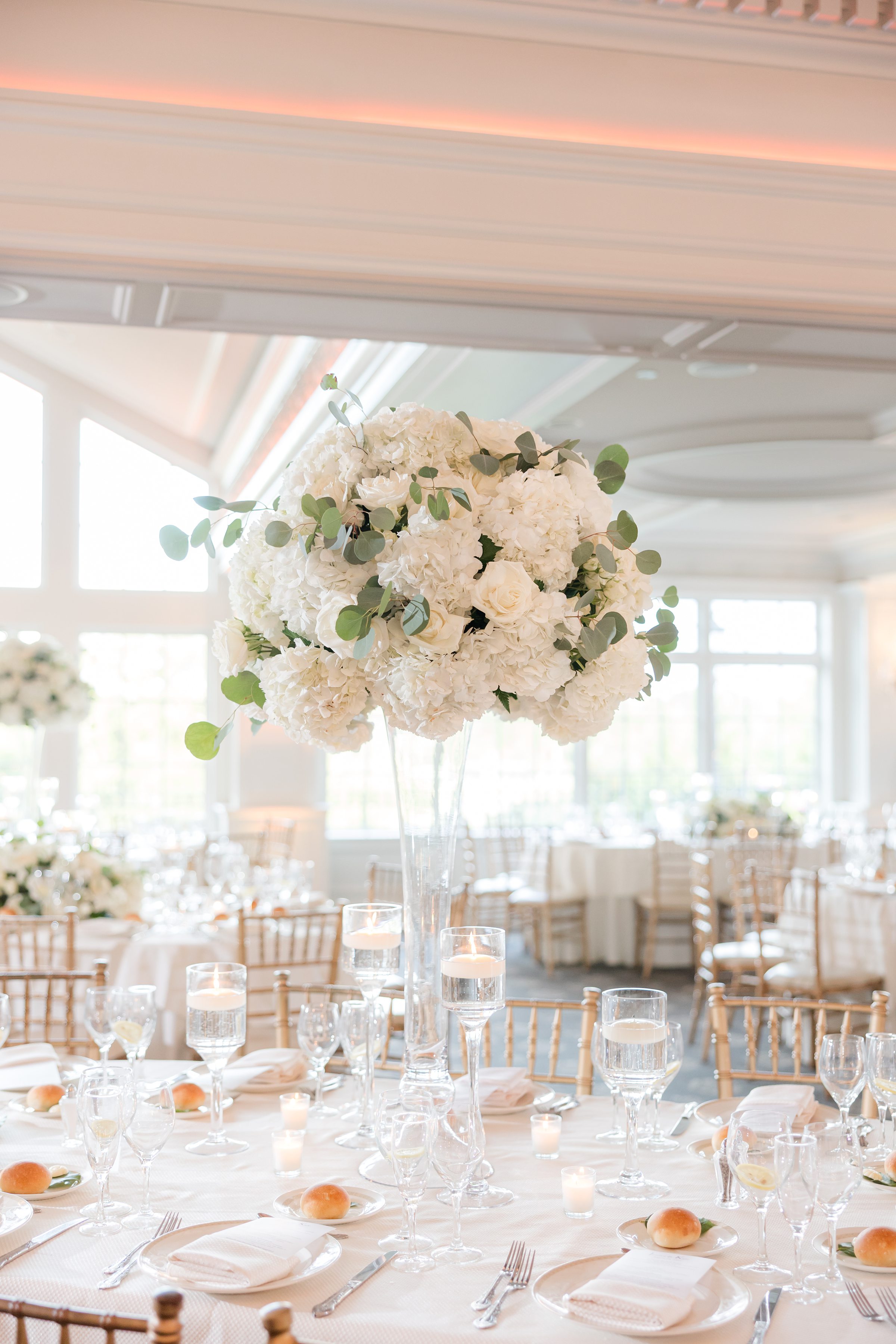 Photo of table decorated with a tall glass vase with white flowers on top, and silver cutlery on the table