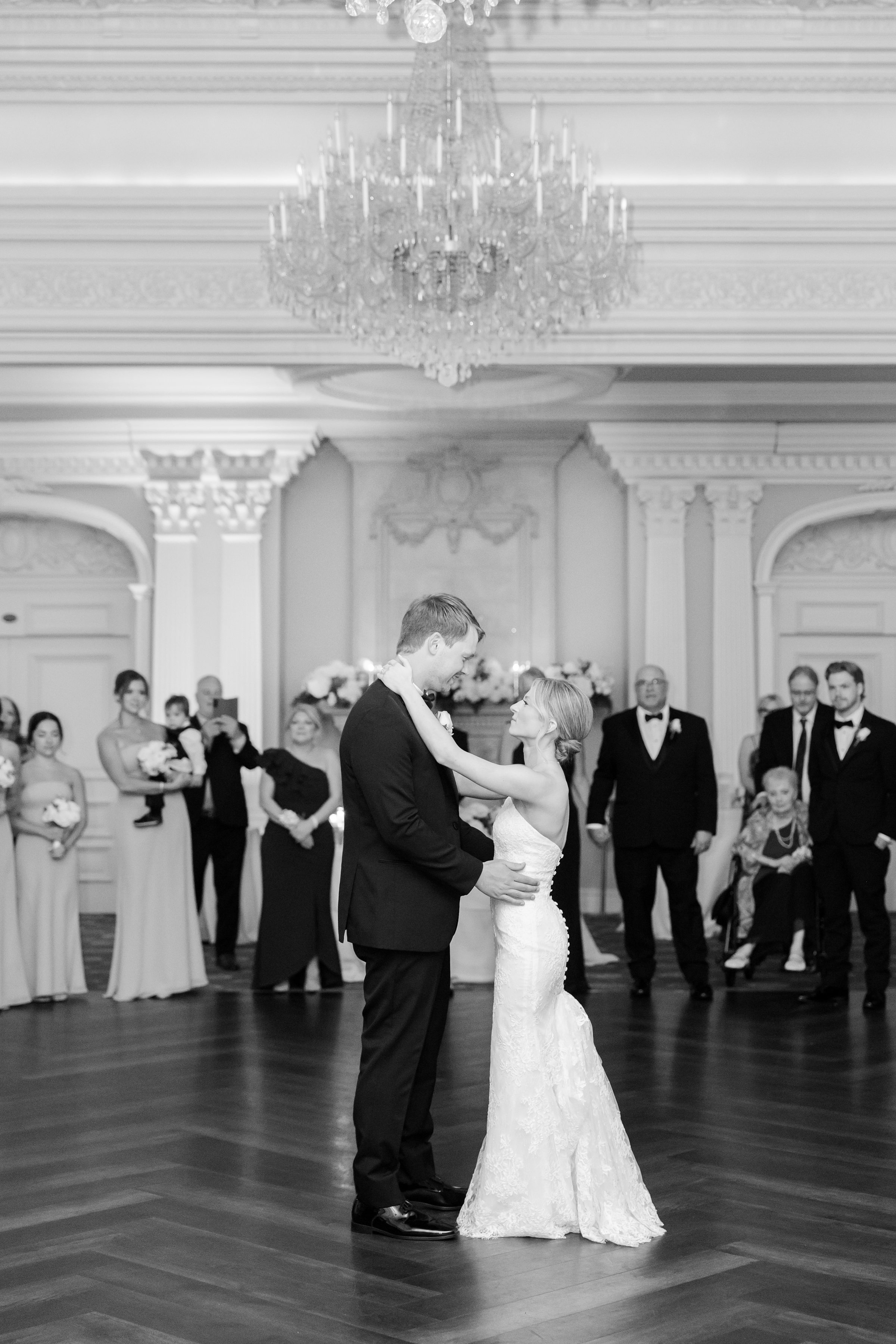 Black and white photo of bride and groom's first dance in the middle of the dancefloor, holding each other