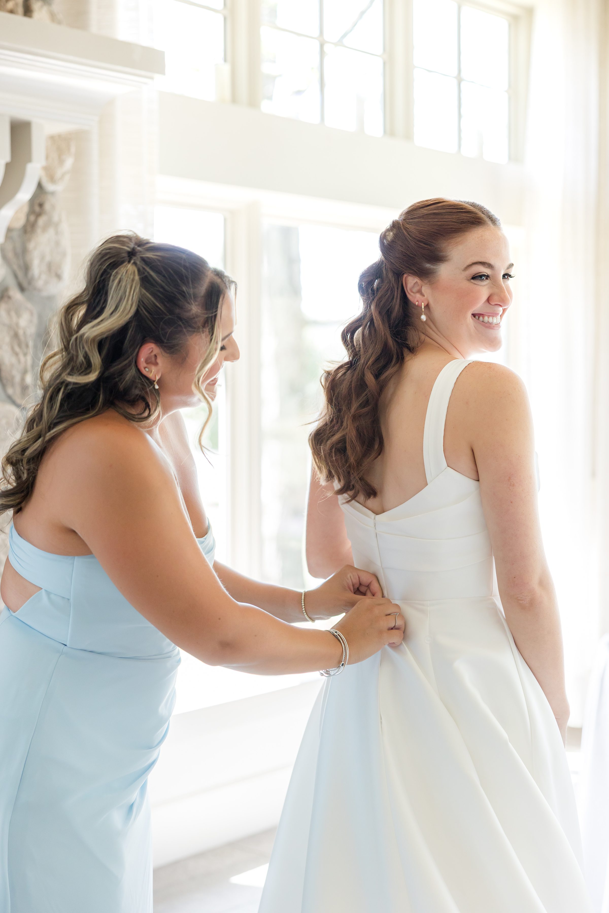 Bride getting ready, while her bridesmaid is helping her zip the gown up