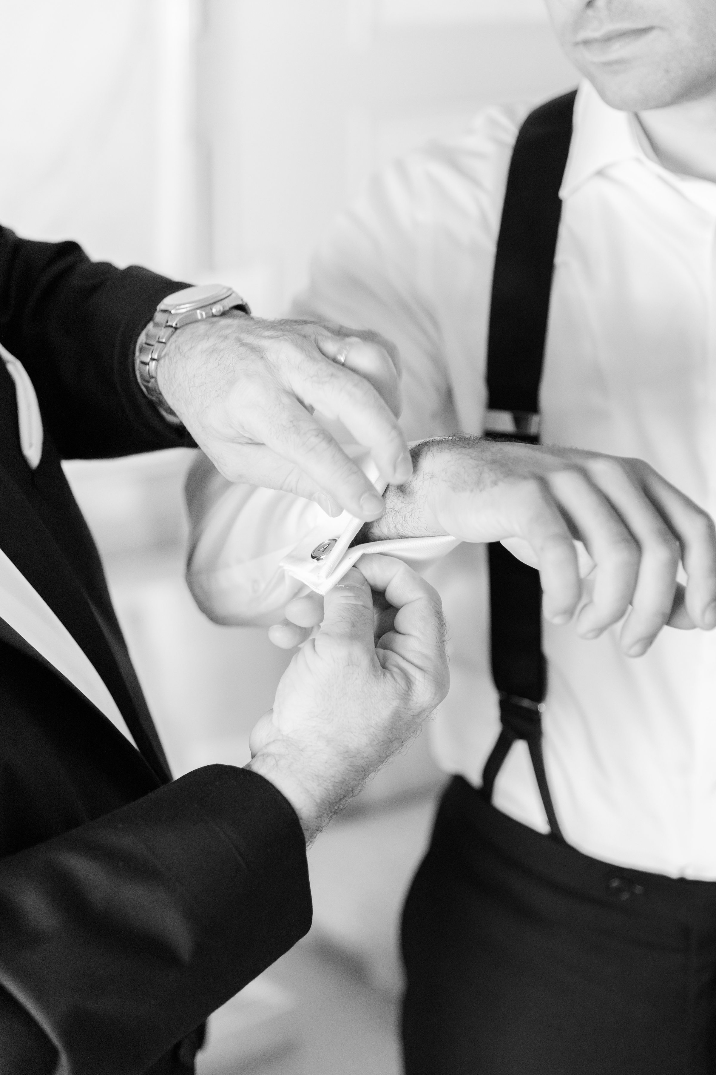 a close-up shot of groomsmen helping the groom fix his wrist buttons, picture is in black and white 