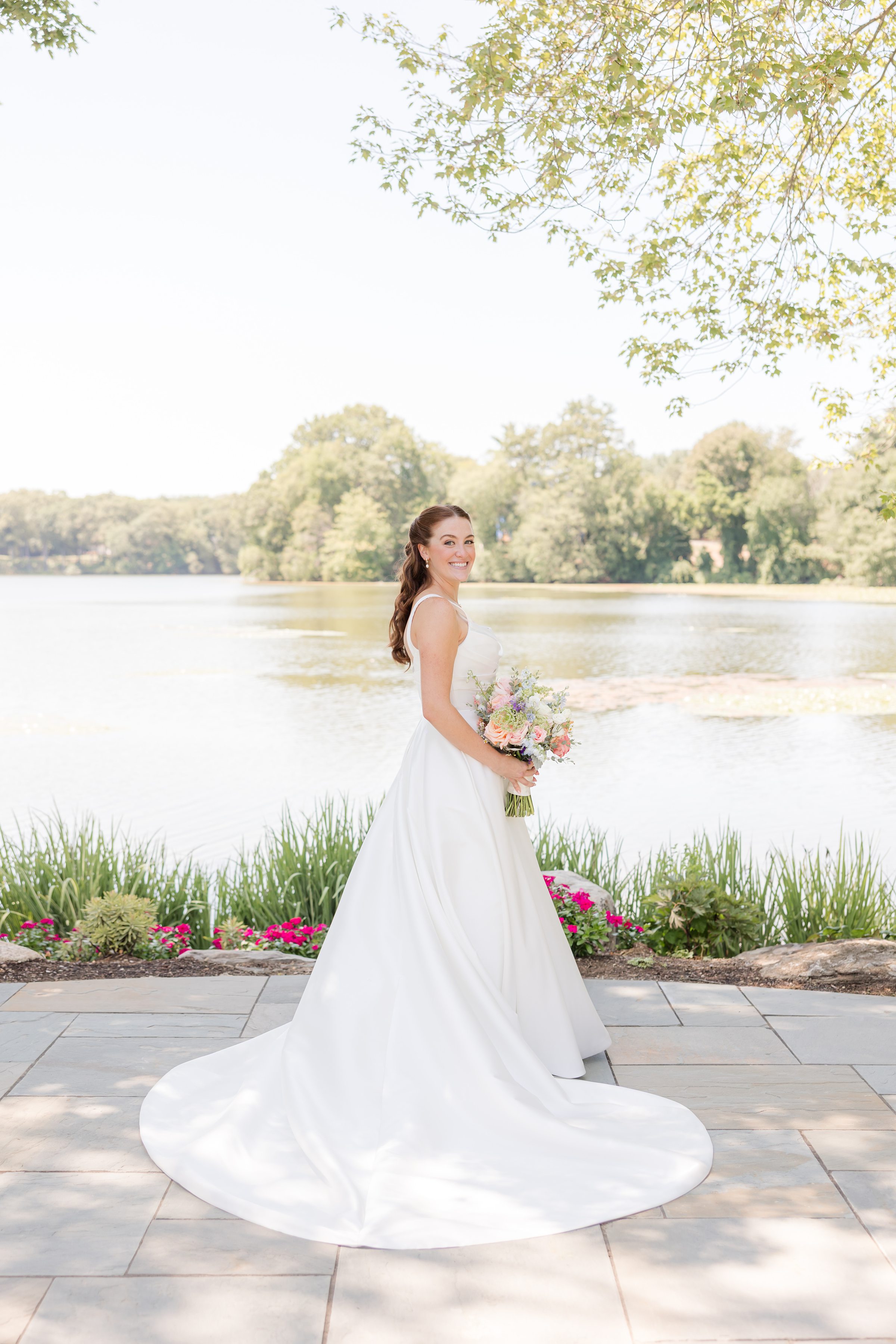 a solo picture of bride with wedding dress in a circular trail while holding a flower bouquet by the lake 