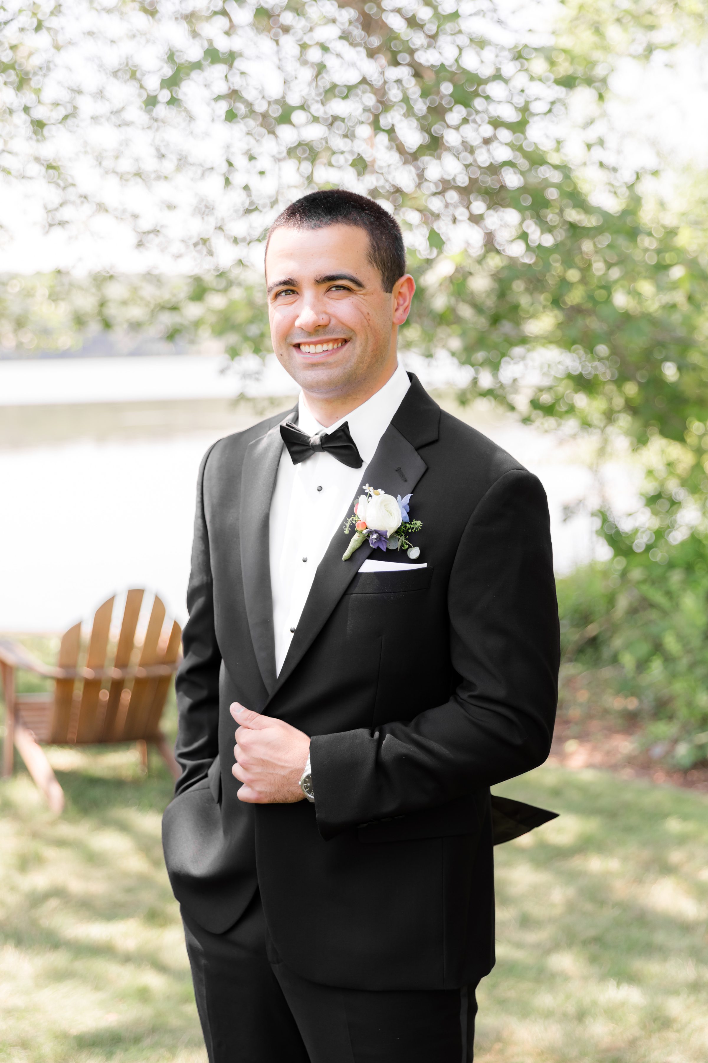 a portrait picture of groom smiling, wearing a black tuxedo 