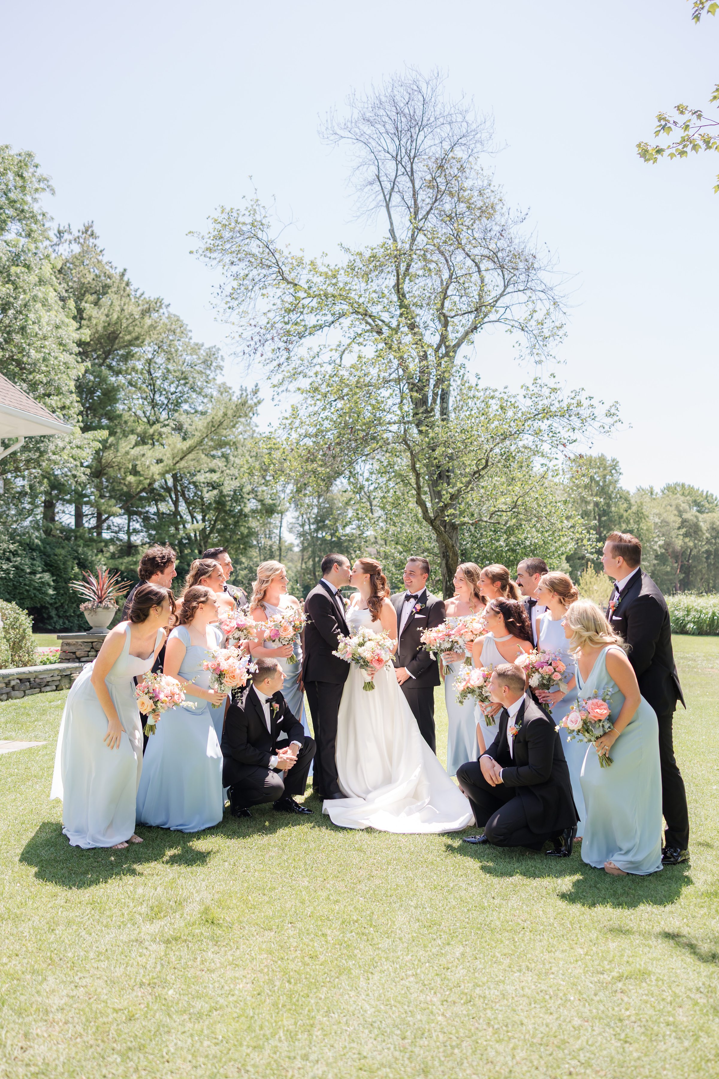 Bride and groom kissing each other while being surrounded by groomsmen and bridesmaids 