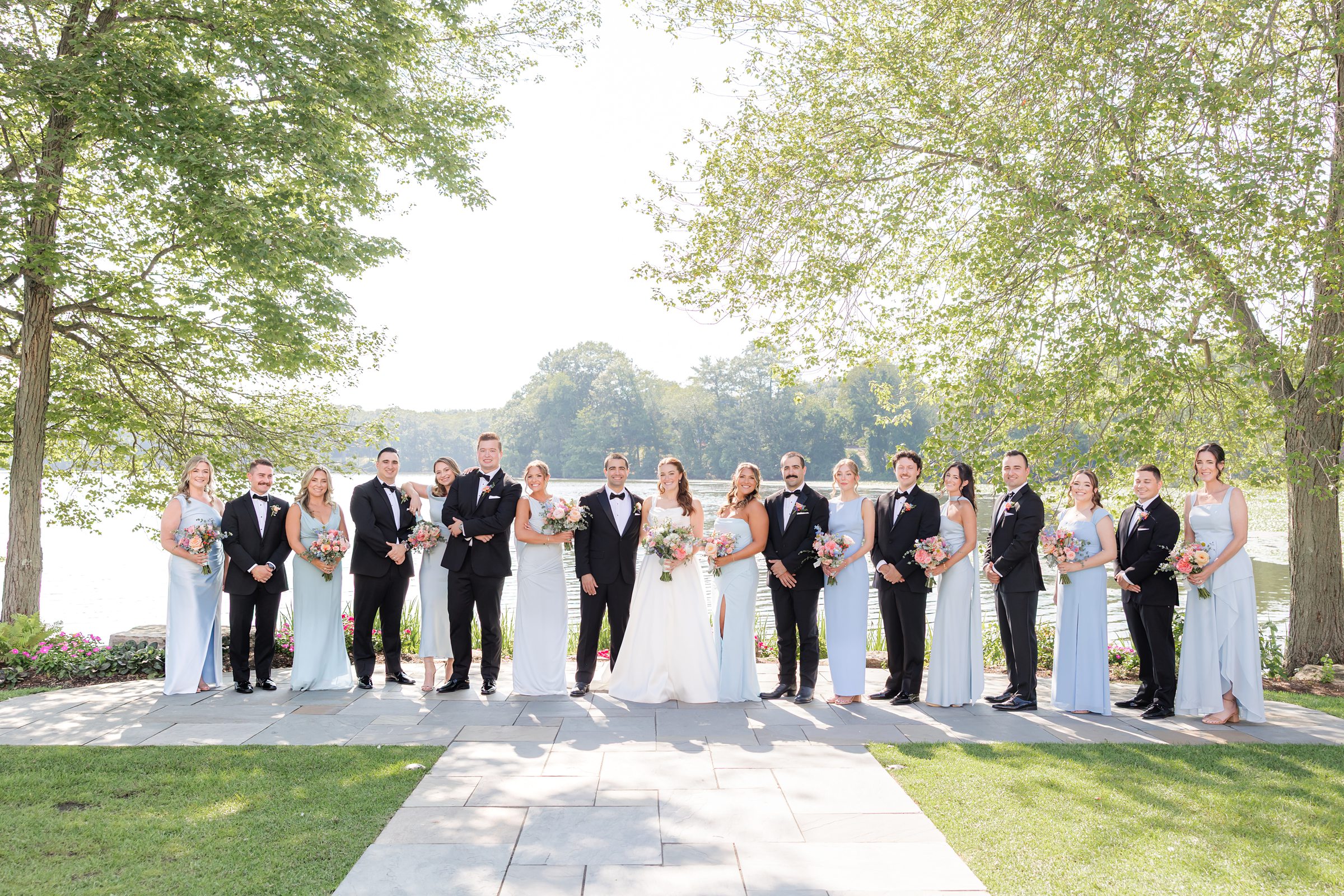 landscape picture of bride and groom with bridesmaids and groomsmen by the lake with trees on each sides