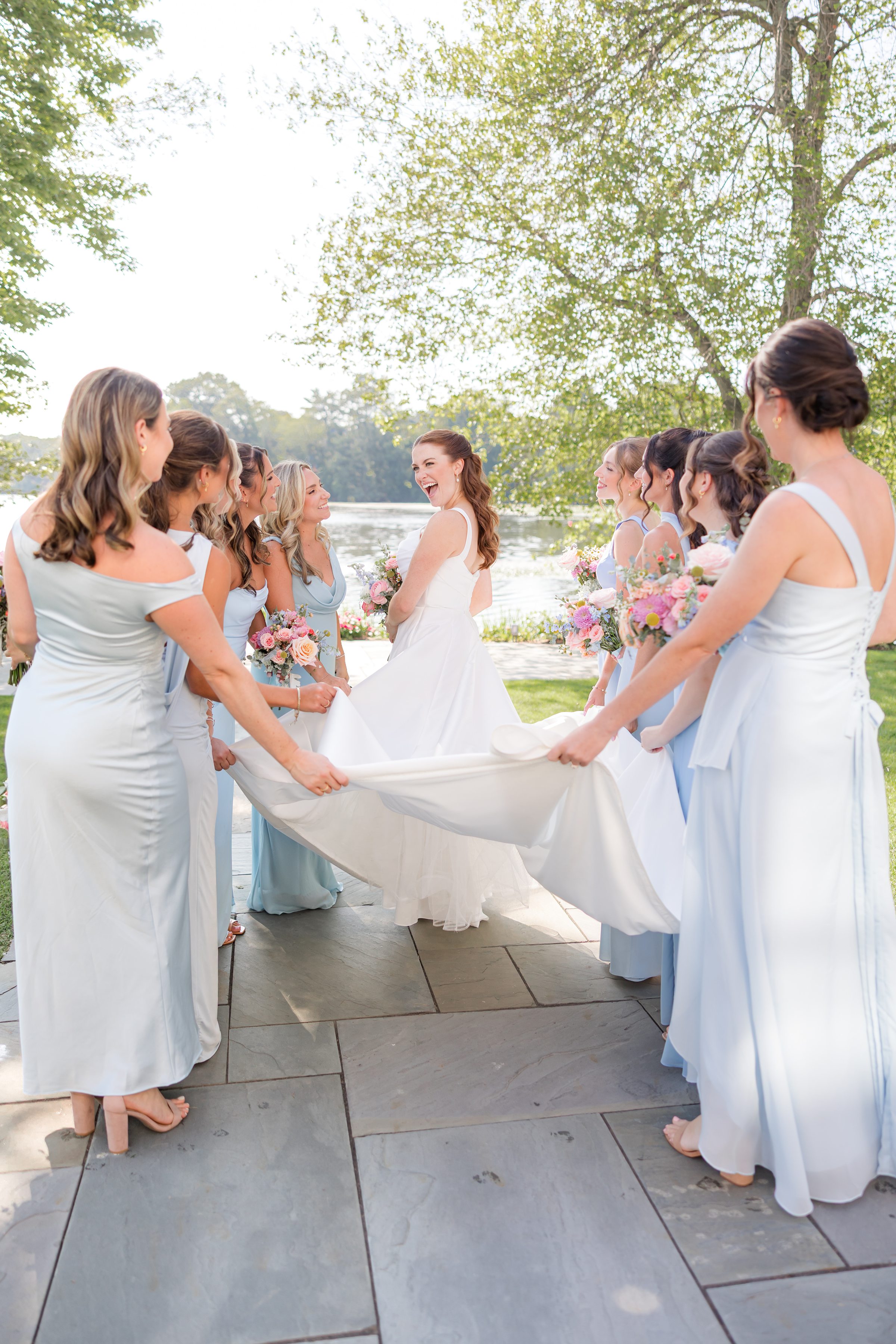 portrait picture of bride while her bridesmaids lift the trail of her dress 