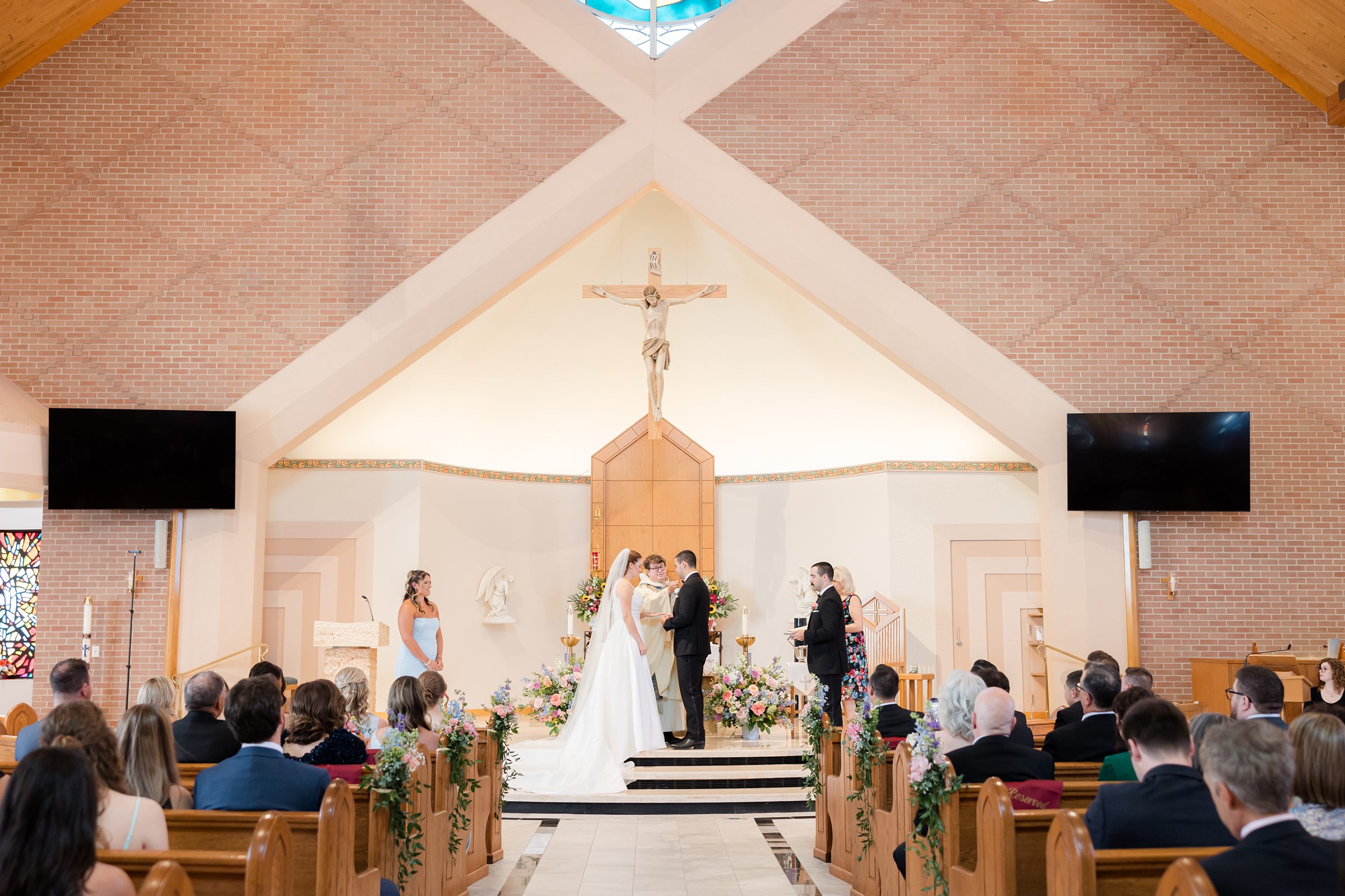 a wide shot of ceremony at St. Elizabeth Church, bride and groom with the priest at the altar, with maid of honor and best man to the side 