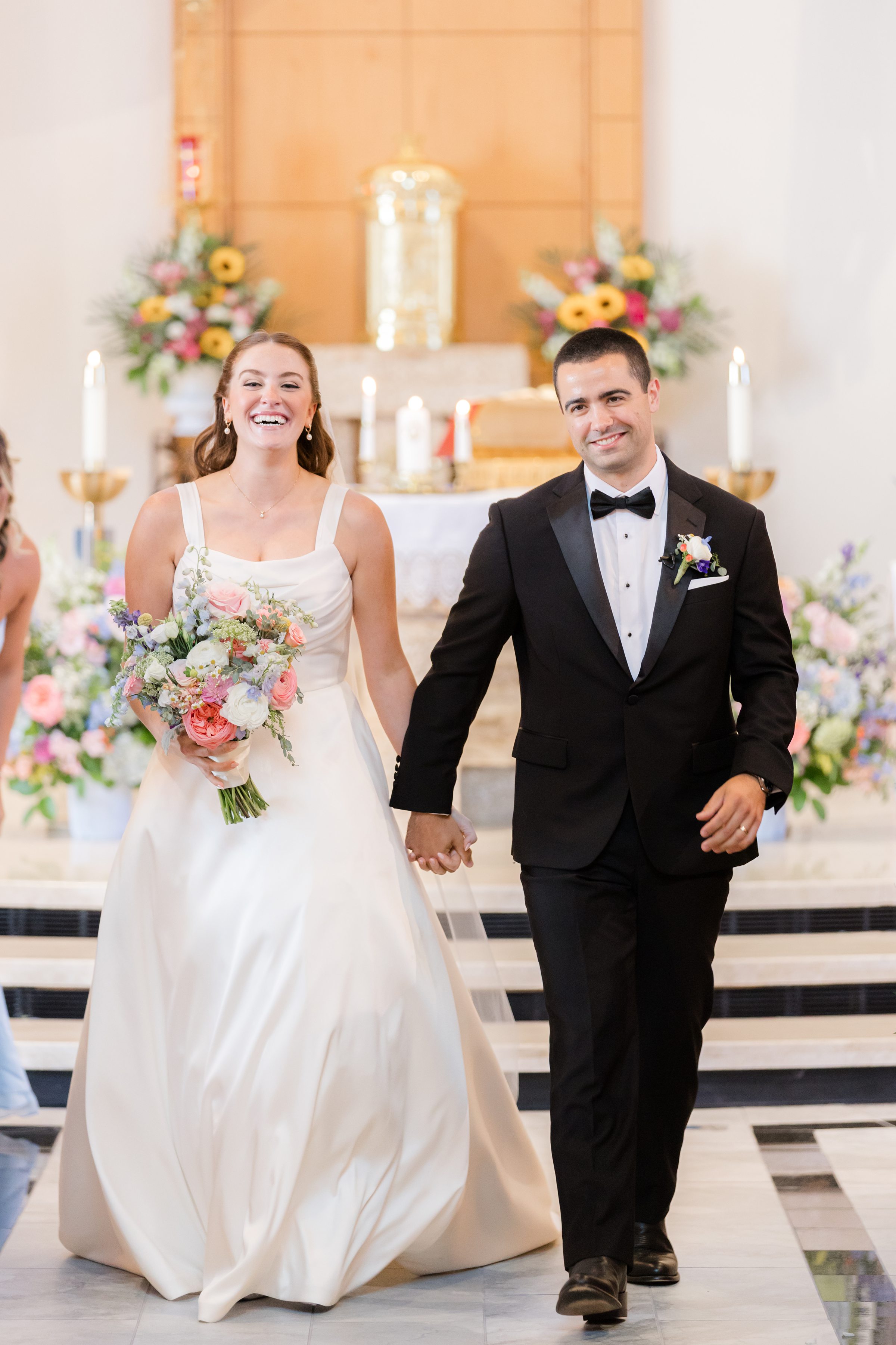a portrait picture of bride and groom walking down the aisle together, bride is holding a flower bouquet