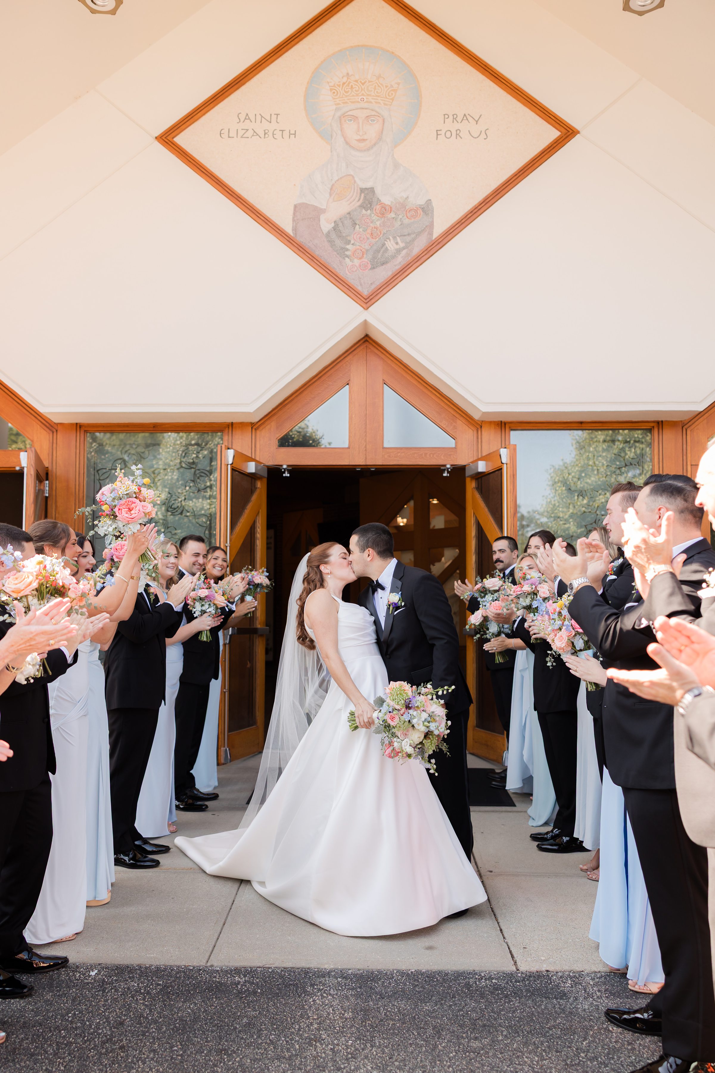 bride and groom kissing each other by the entrance of St. Elizabeth Church, while guests are cheering for them 