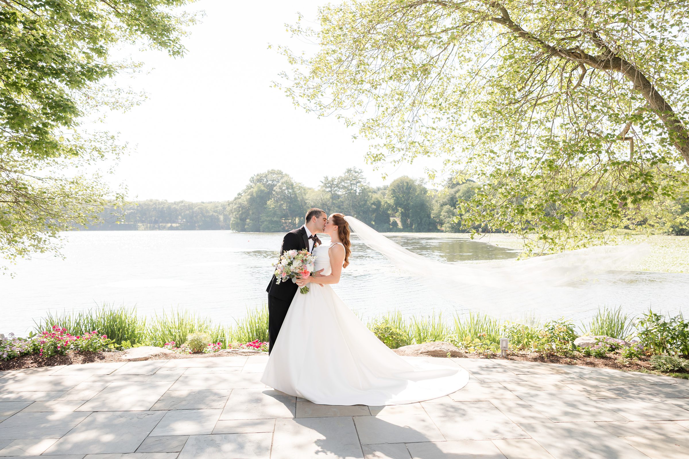 a landscape picture of bride and groom kissing by the lake with veil blowing to the side