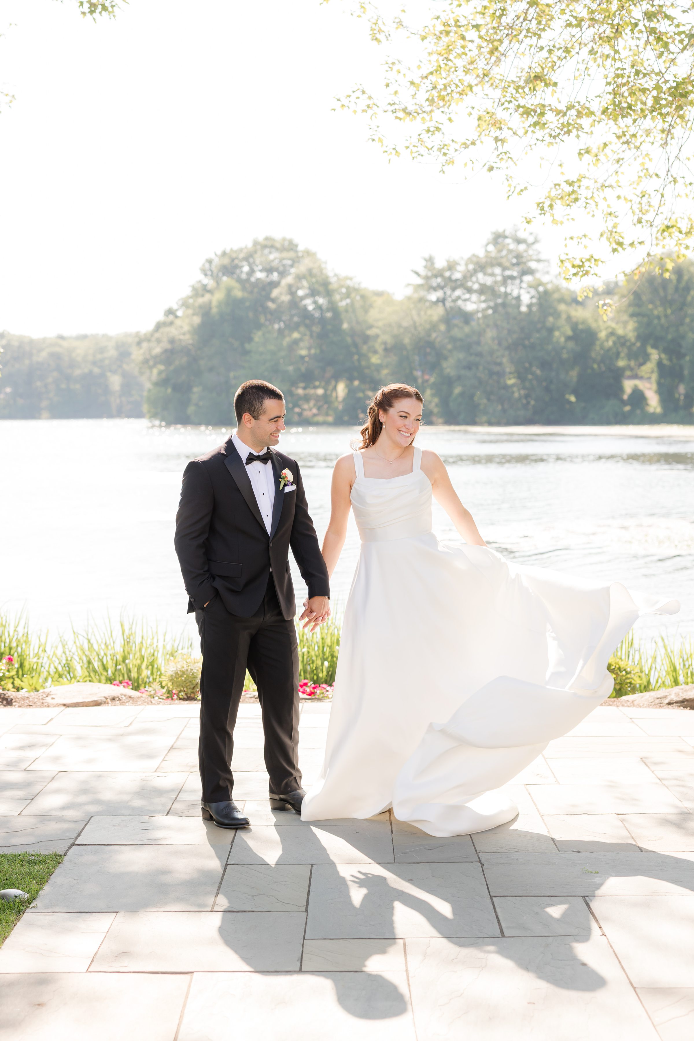 portrait picture of bride and groom standing by the lake, while bride is twirling her dress 
