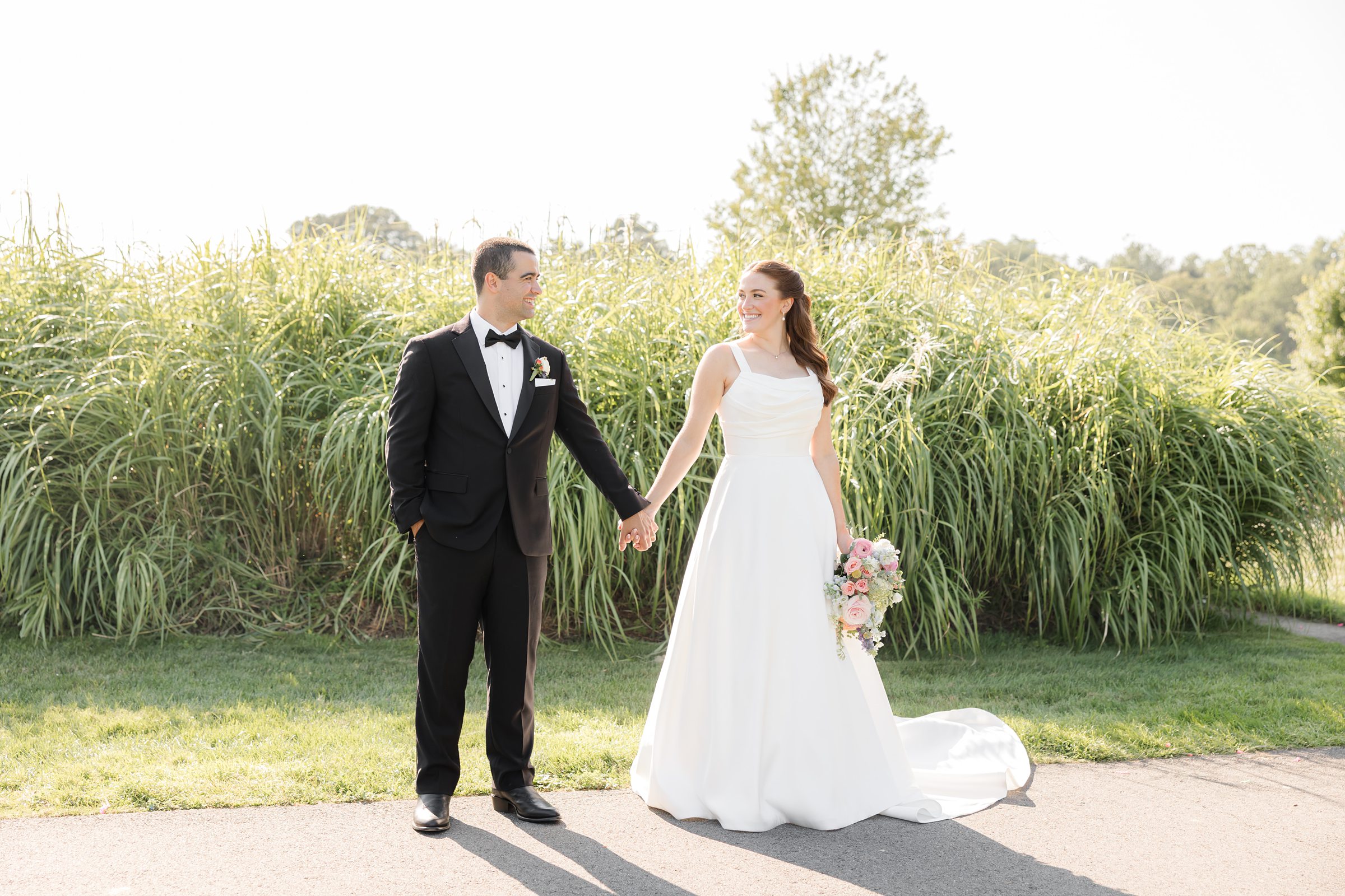 landscape picture of bride and groom holding hands with the green plants in the back