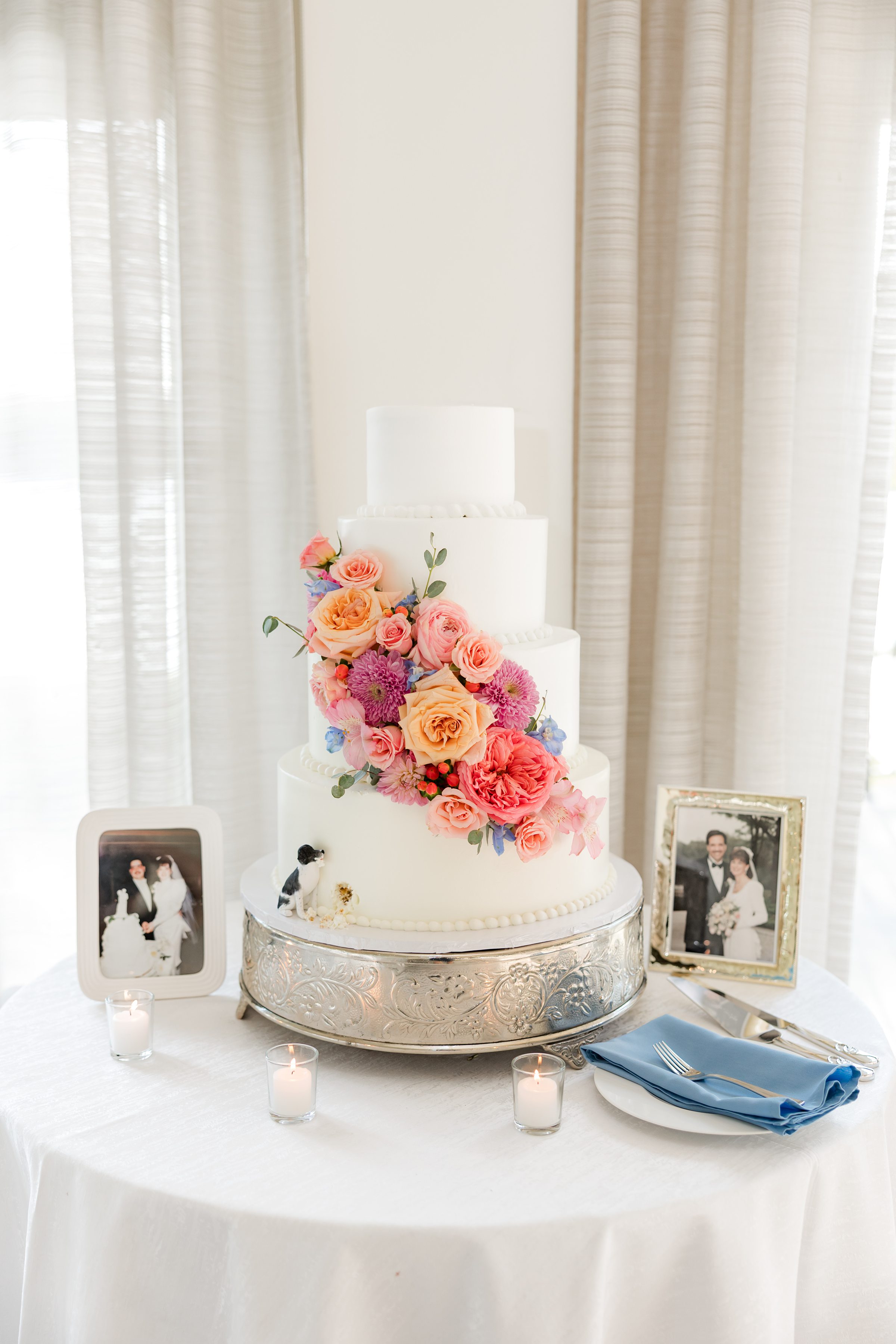 photo of the 4-tier white wedding cake with orange, yellow, pink, powder blue flowers, with bride and groom's parents' pictures on the sides