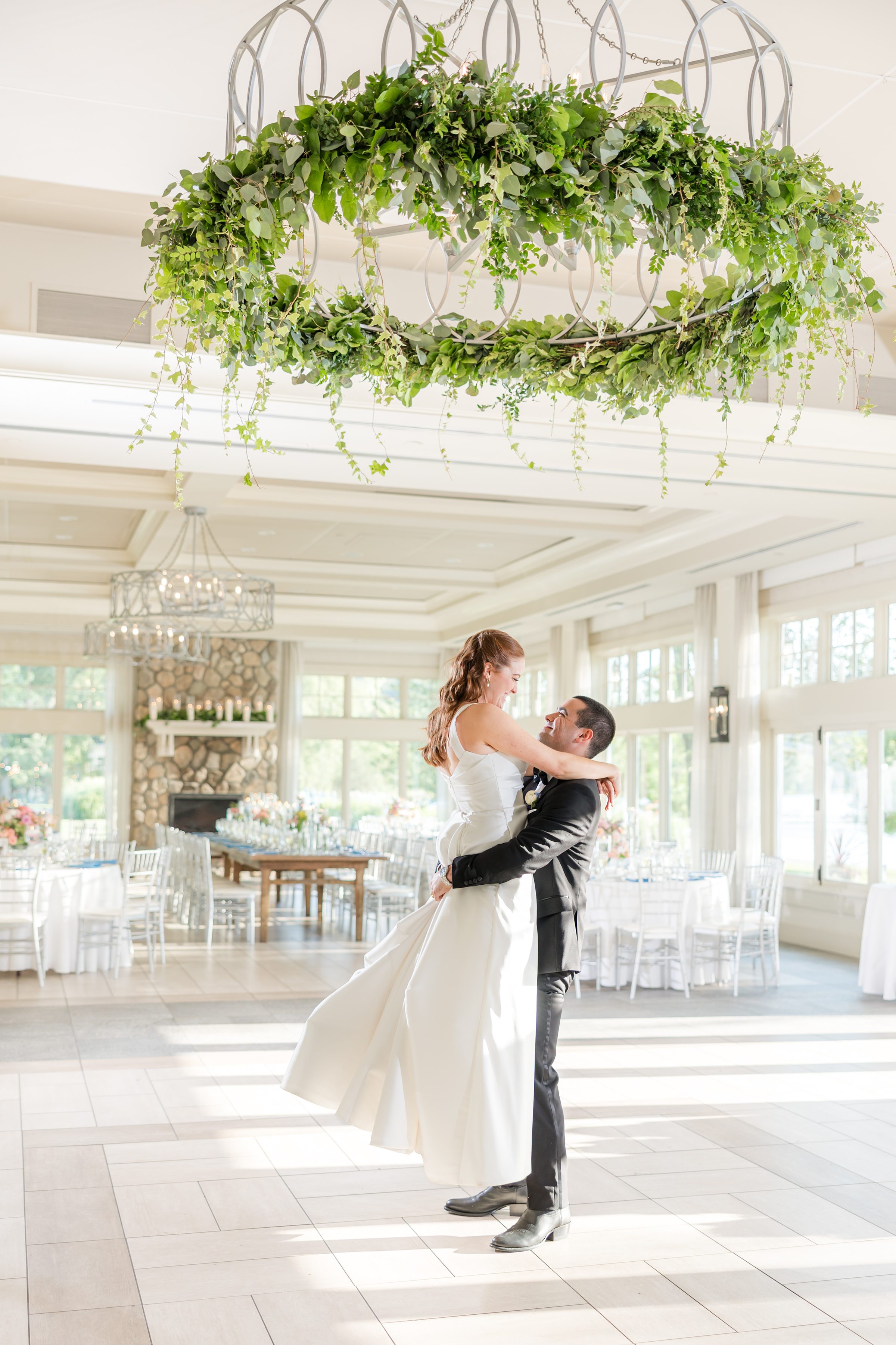 bride and groom rehearsing in an empty ball room, groom is lifting the bride with plant chandelier at the top