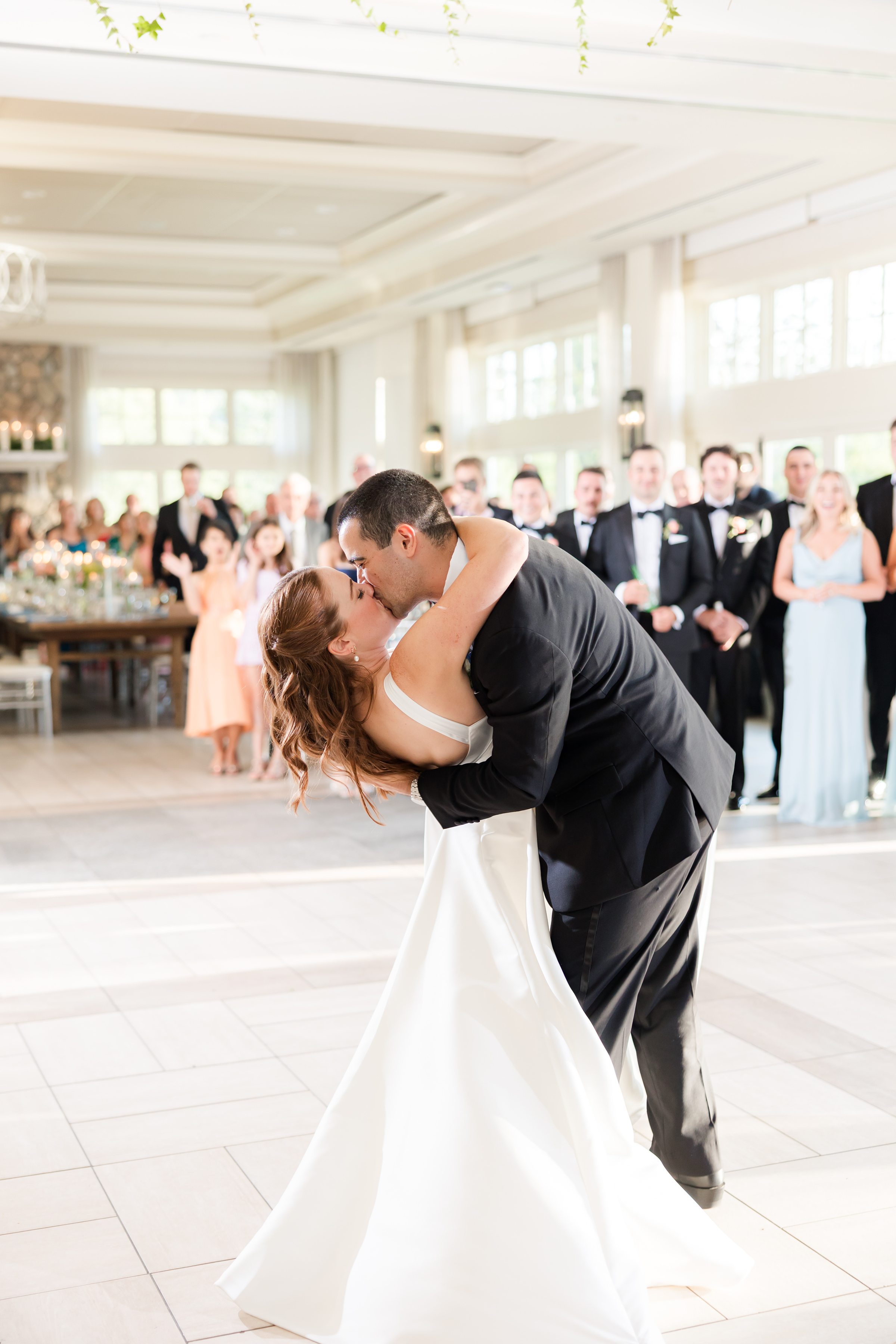 portrait photo of bride and groom dancing while taking a dip in front of the guests
