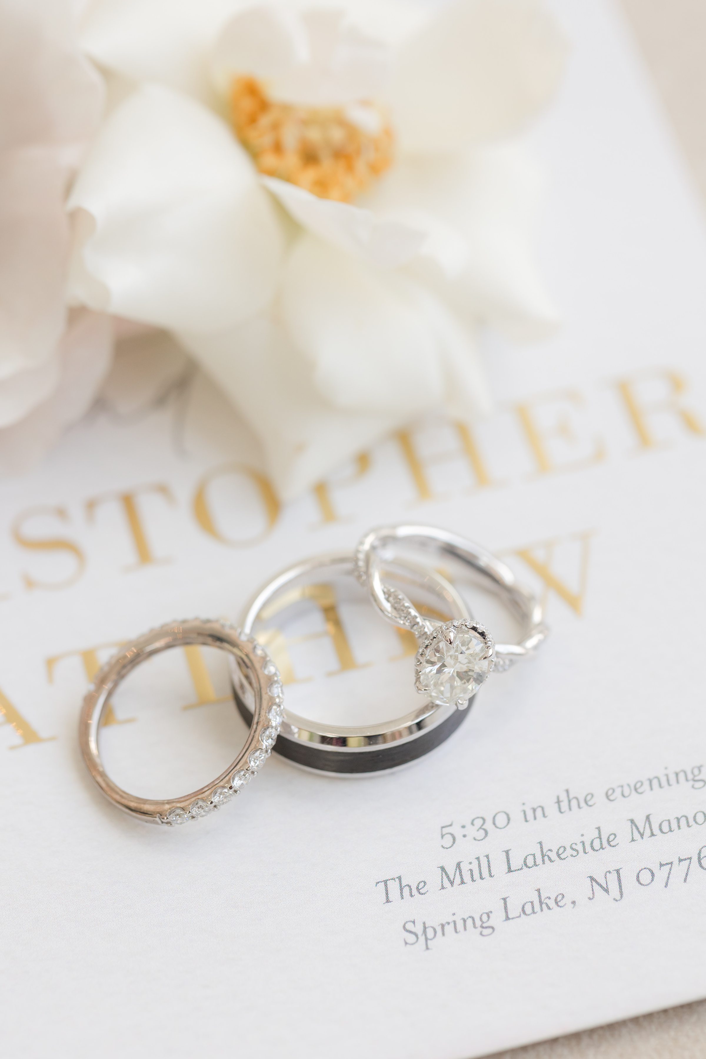 Wedding rings on an invitation card with soft white flowers in the background.