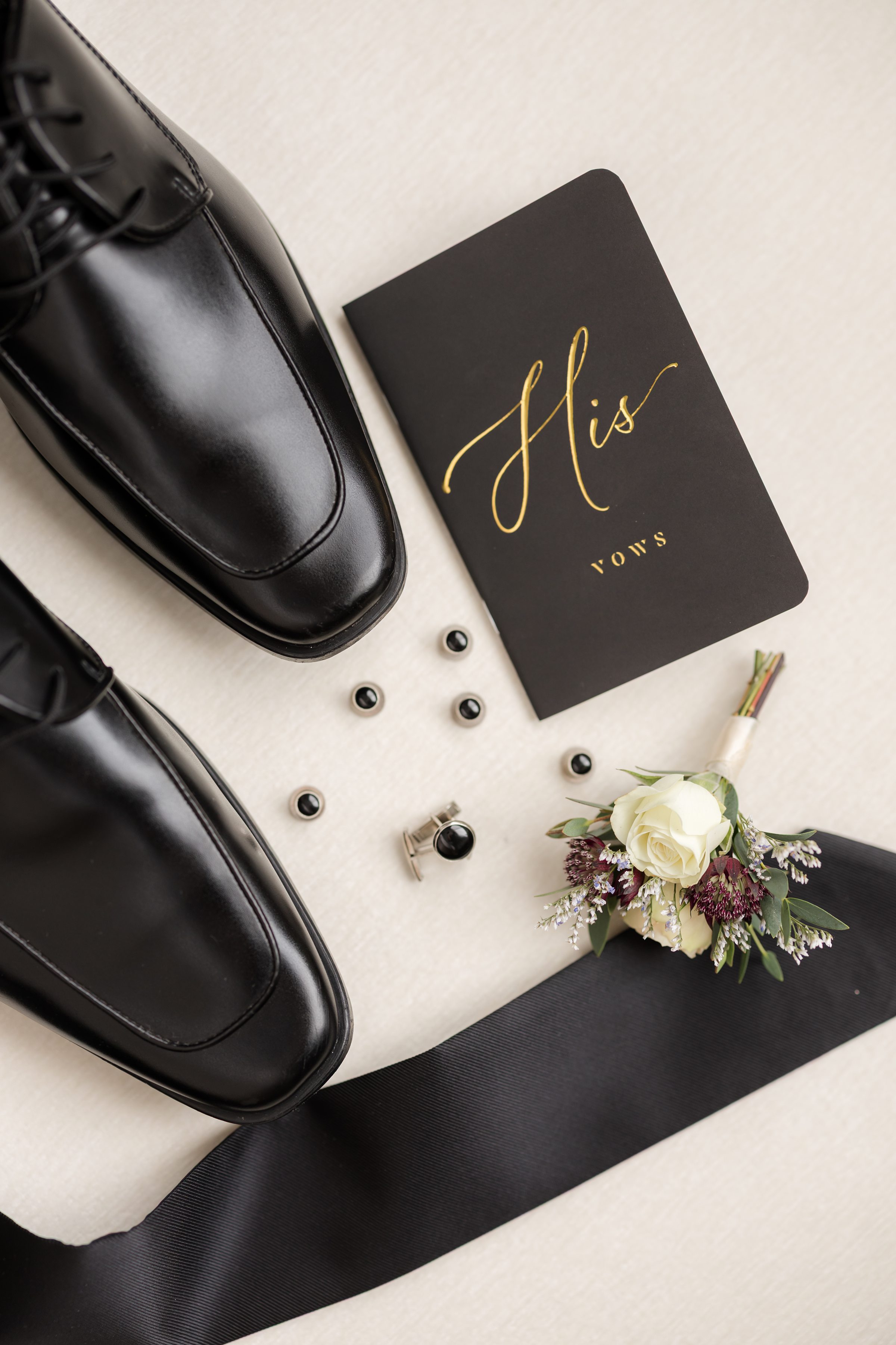 Groom black dress shoes, cufflinks, boutonniere, tie, and vow book.