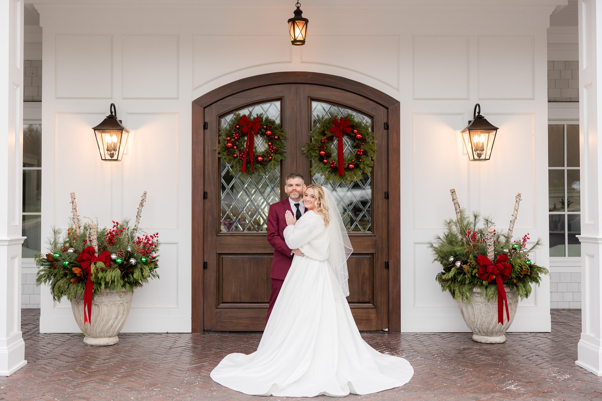 Bride and groom embrace in front of festive doors adorned with holiday wreaths