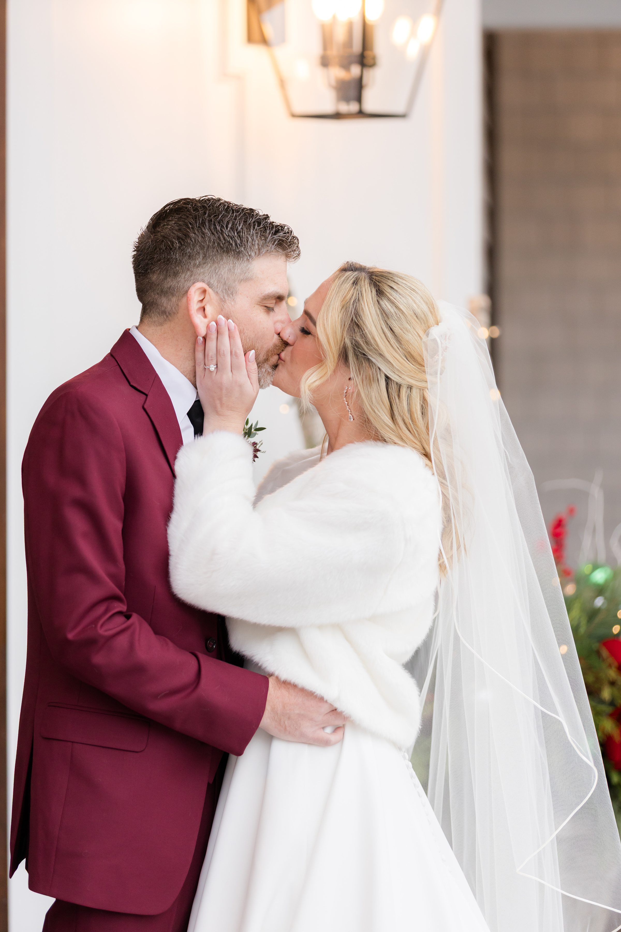 Bride and groom share a close, tender kiss, her hand gently resting on his face.