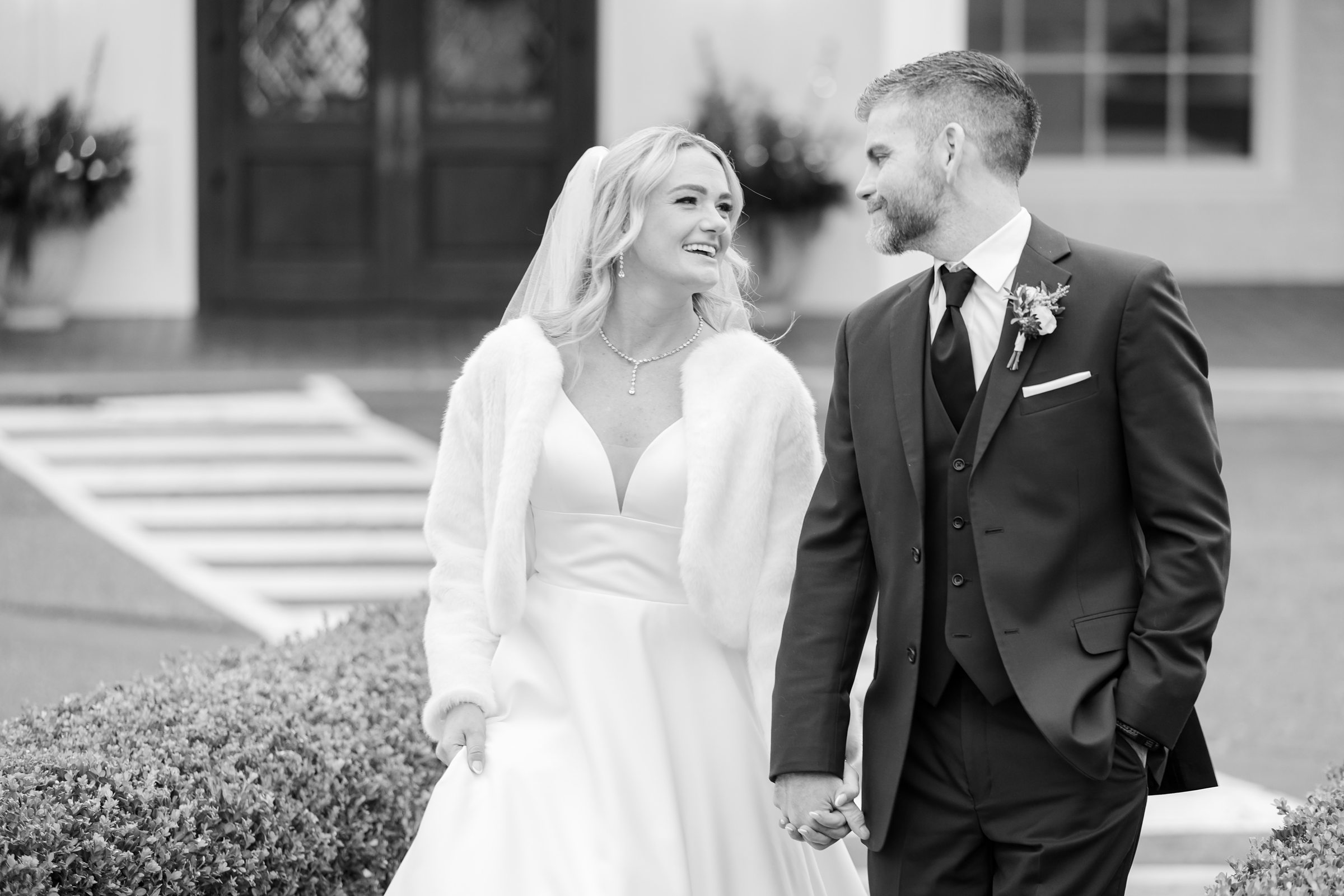 Bride and groom walk together, smiling at each other in a soft black-and-white moment.