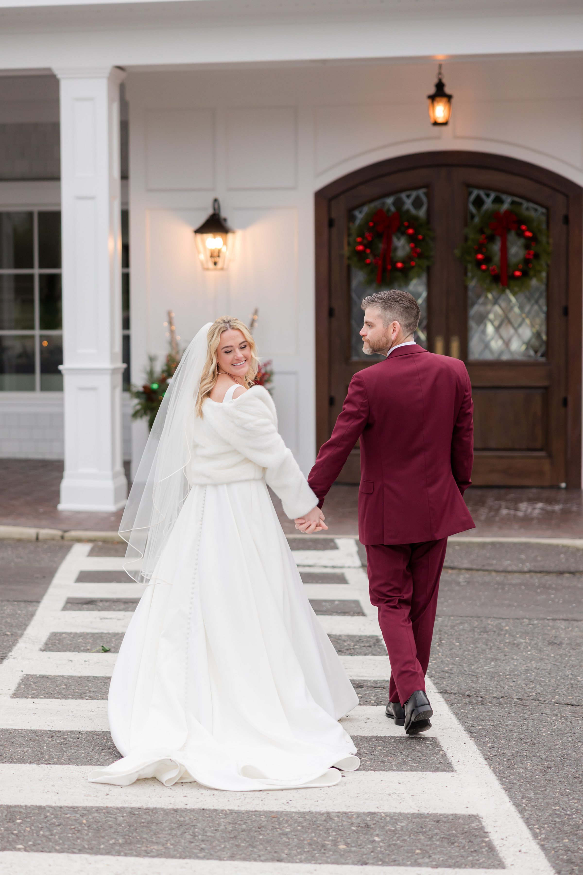 Bride and groom walk together, glancing back with joyful smiles in front of festive doors.
