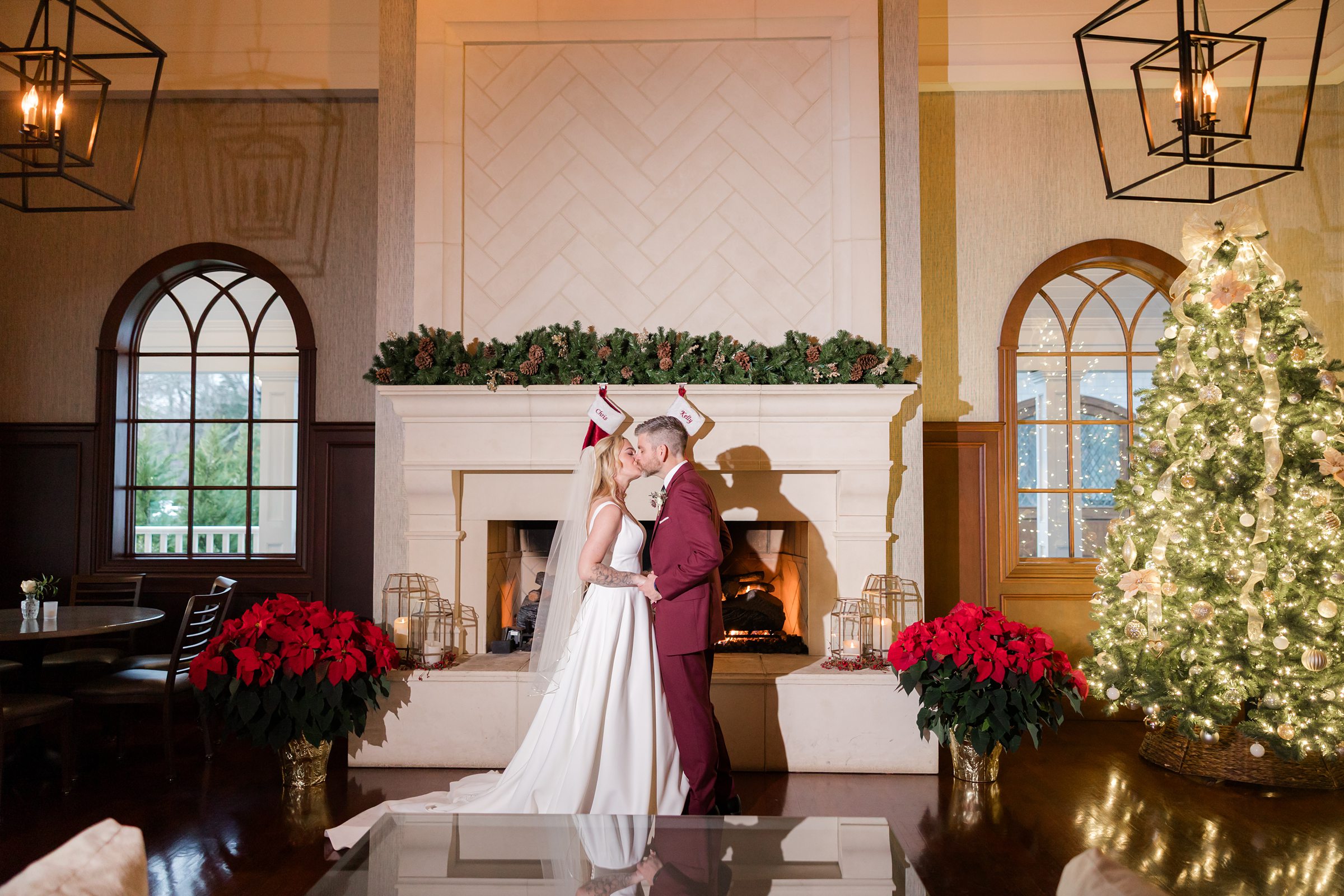 Bride and groom share a kiss in front of a cozy fireplace and glowing christmas tree.