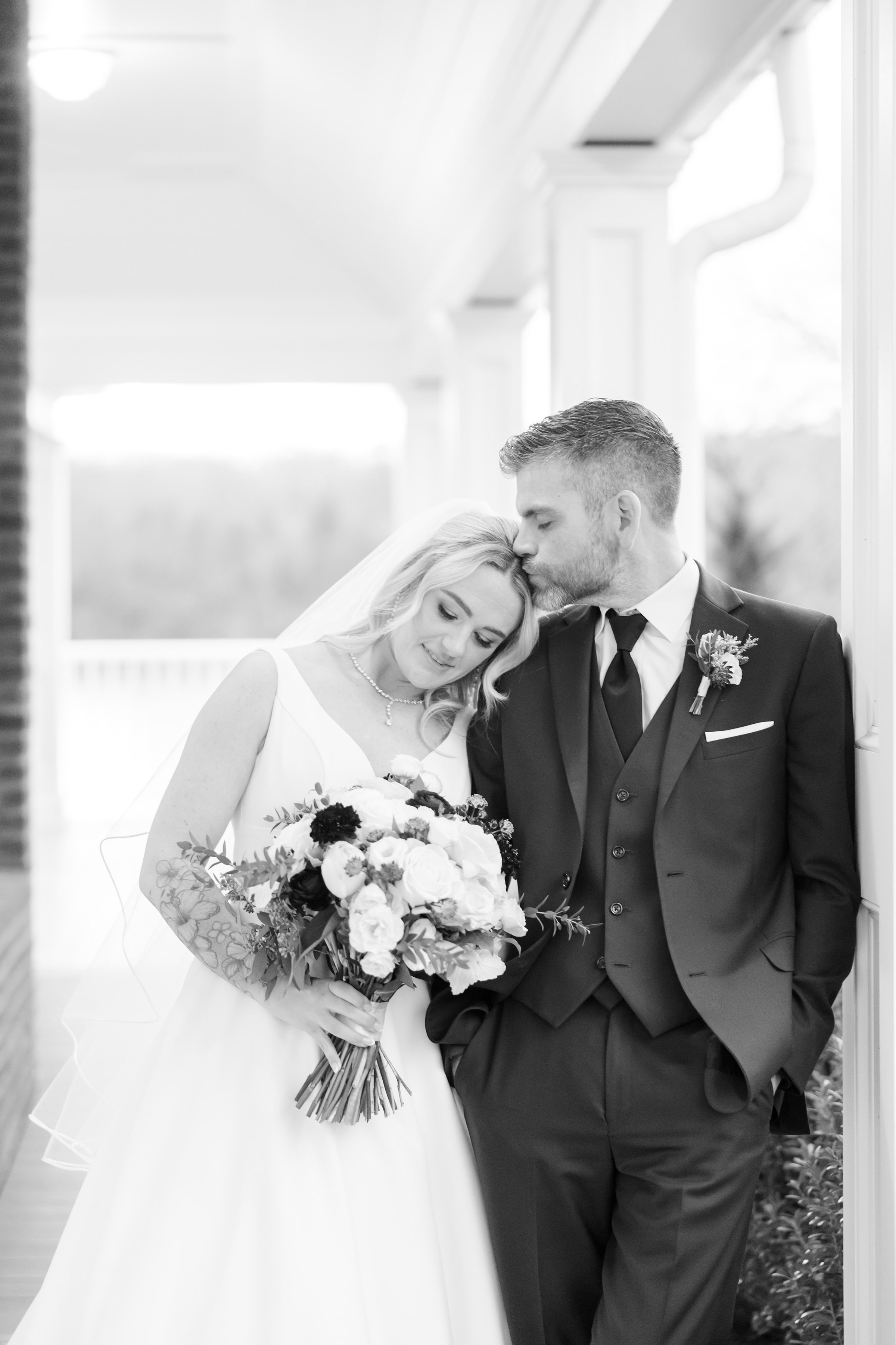 Groom kissing the bride’s forehead as she holds her bouquet.