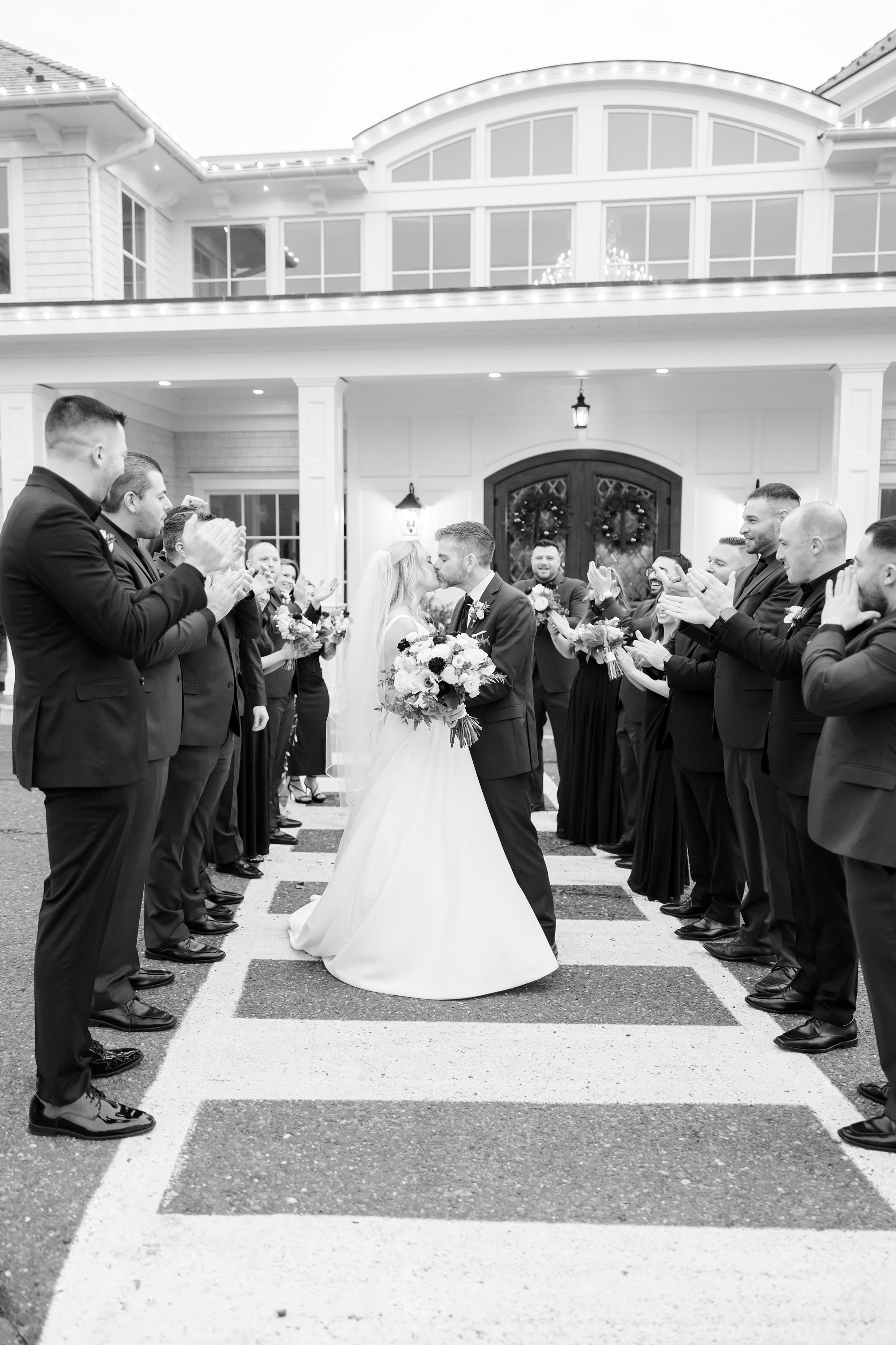 Bride and groom shares a kiss outside the venue as their wedding party cheers, celebrating love in a joyful winter scene.