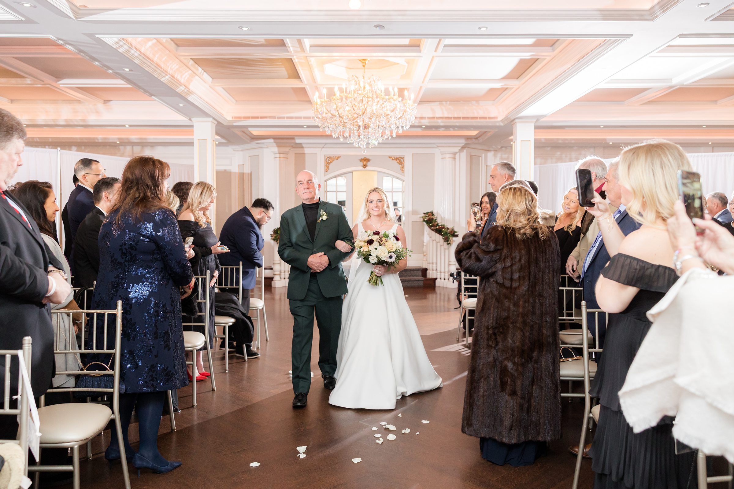 Bride walks down the aisle with her father, holding a bouquet and smiling as guests stand on either side, capturing a heartfelt and emotional ceremony moment.