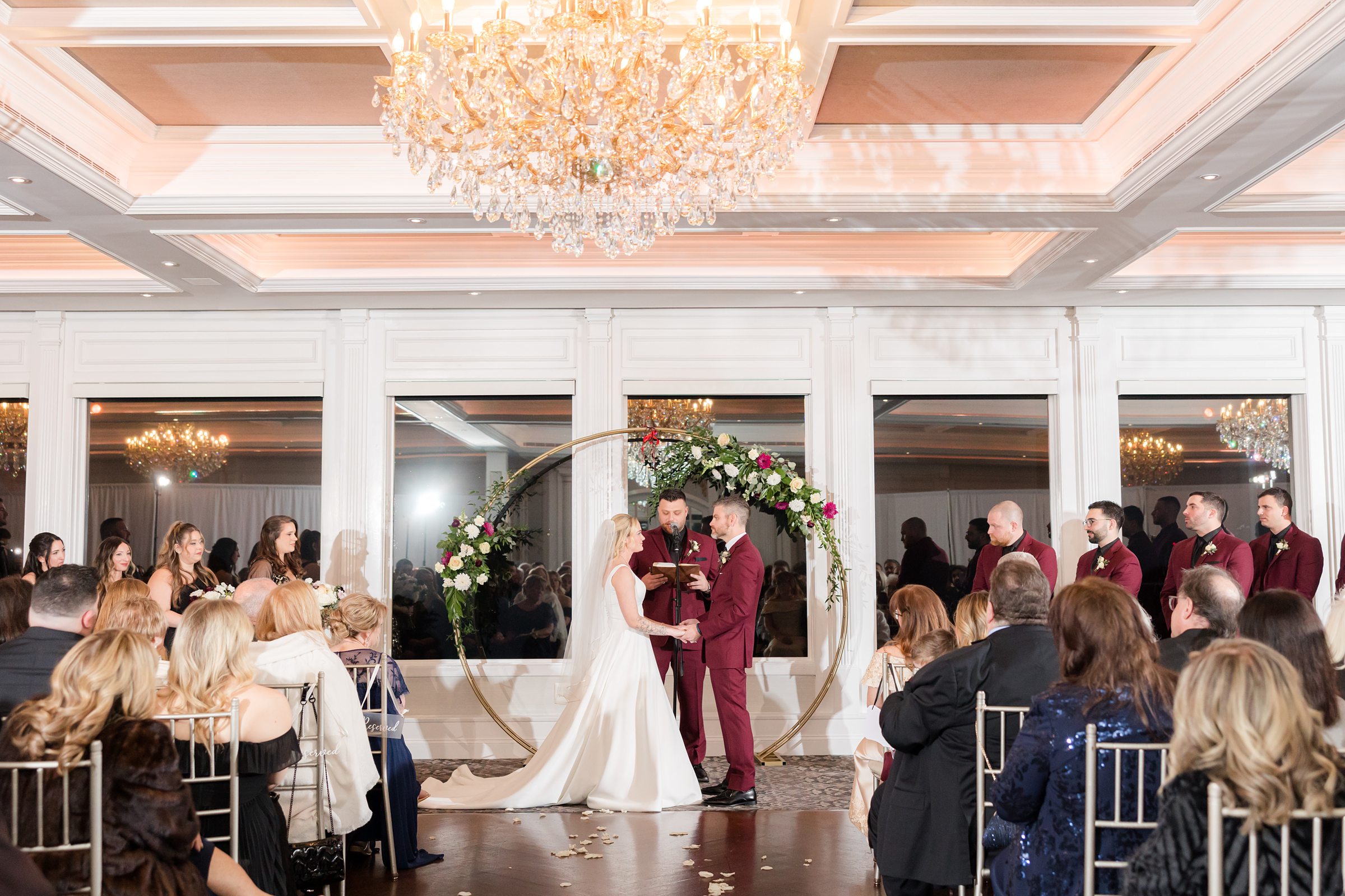 Bride and groom stands together at the altar, surrounded by family and friends, in a warm and elegant ceremony setting.