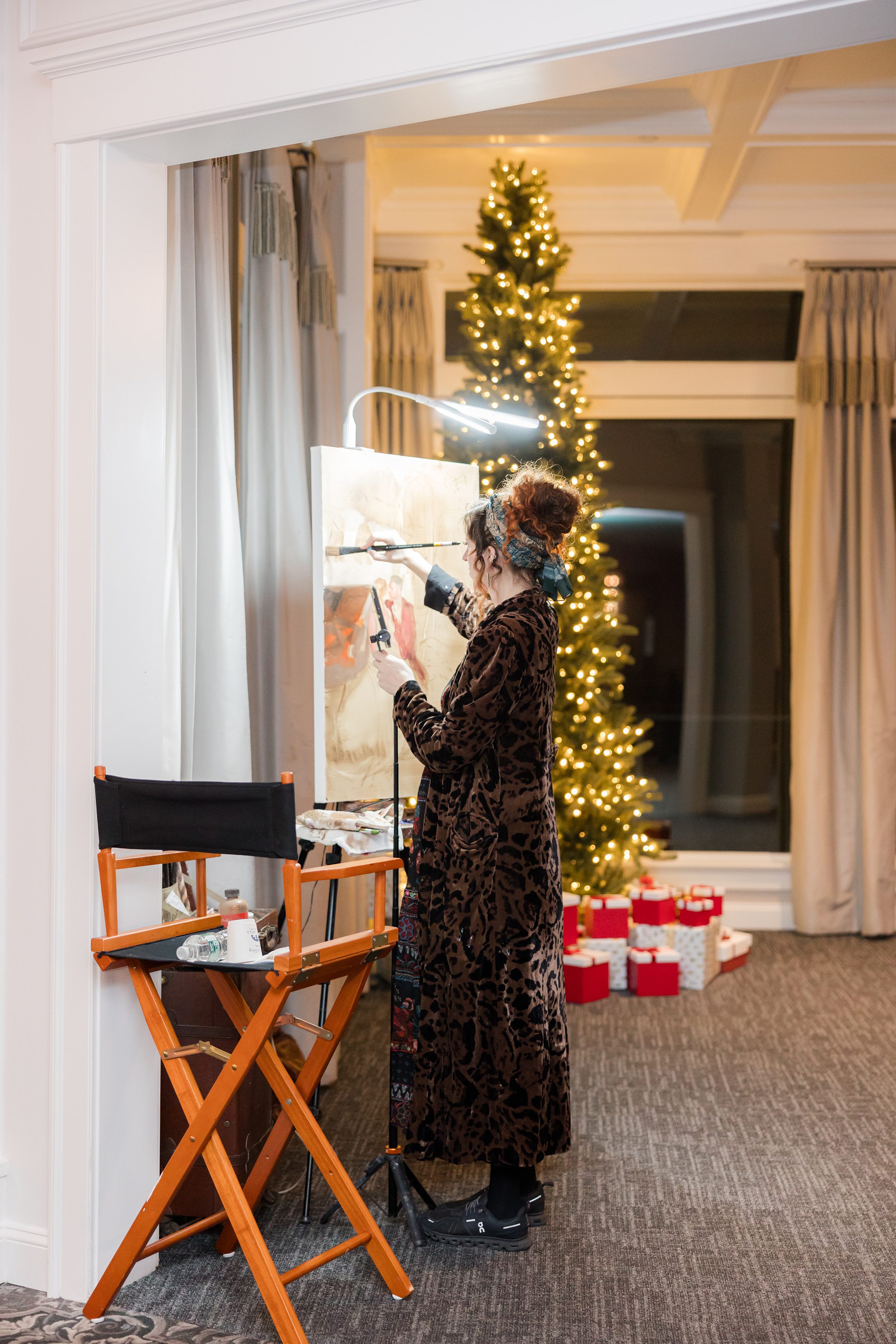 Artist painting live at the wedding while a softly lit Christmas tree glows in the background.