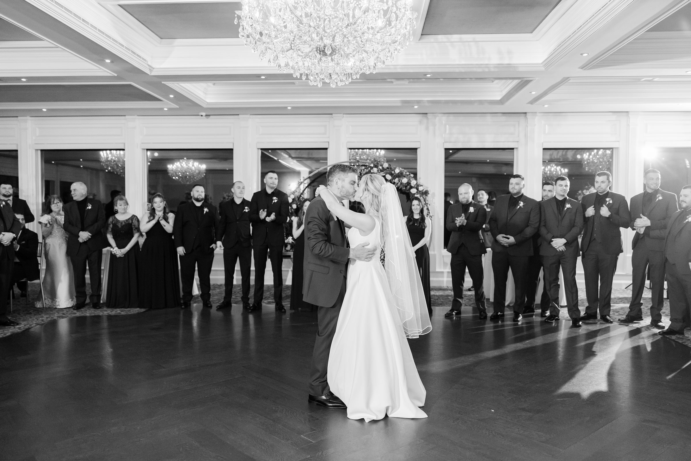 Bride and groom sharing a romantic first dance at the center of the ballroom, surrounded by guests watching and applauding.