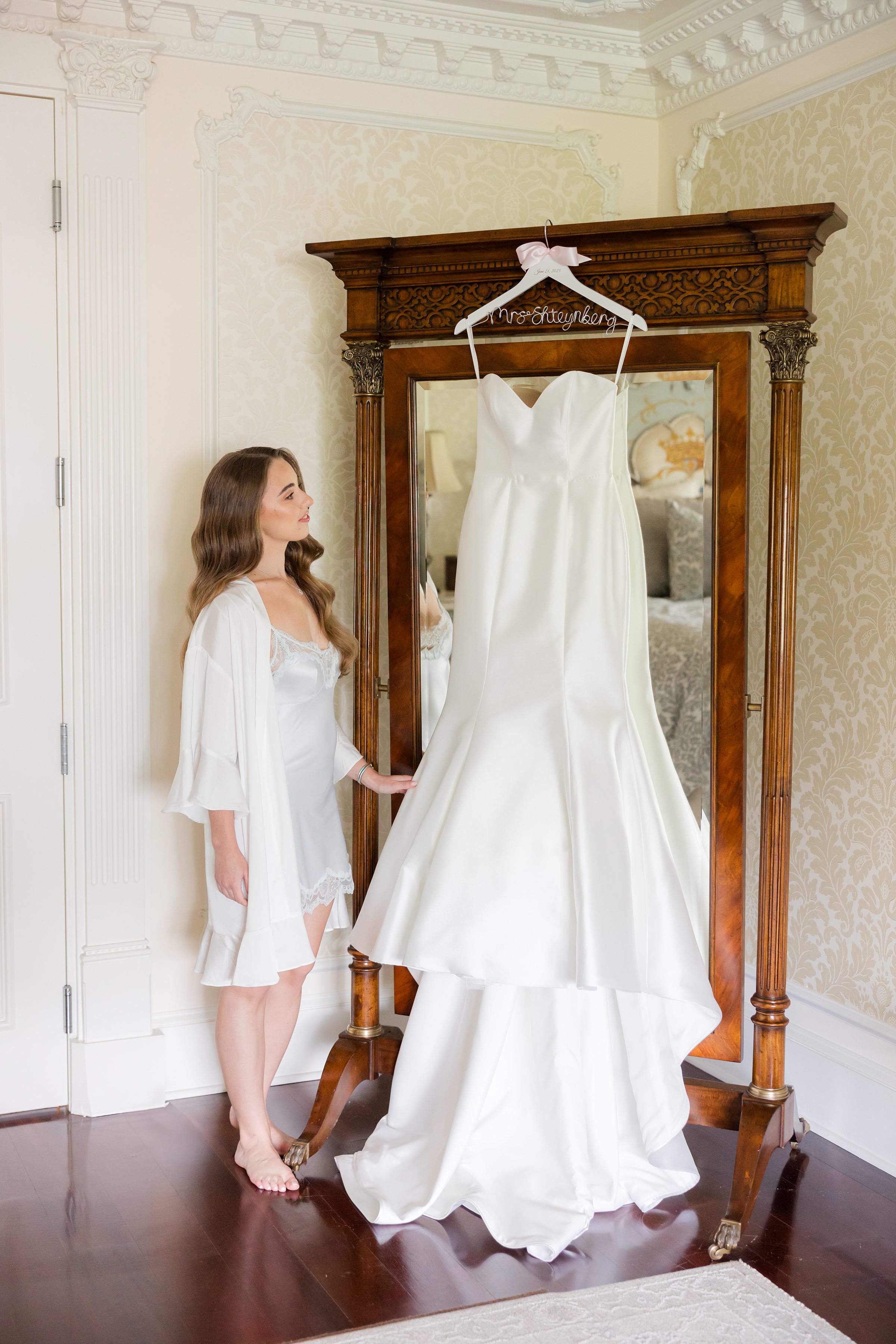 Bride looking at her wedding dress hung above the mirror