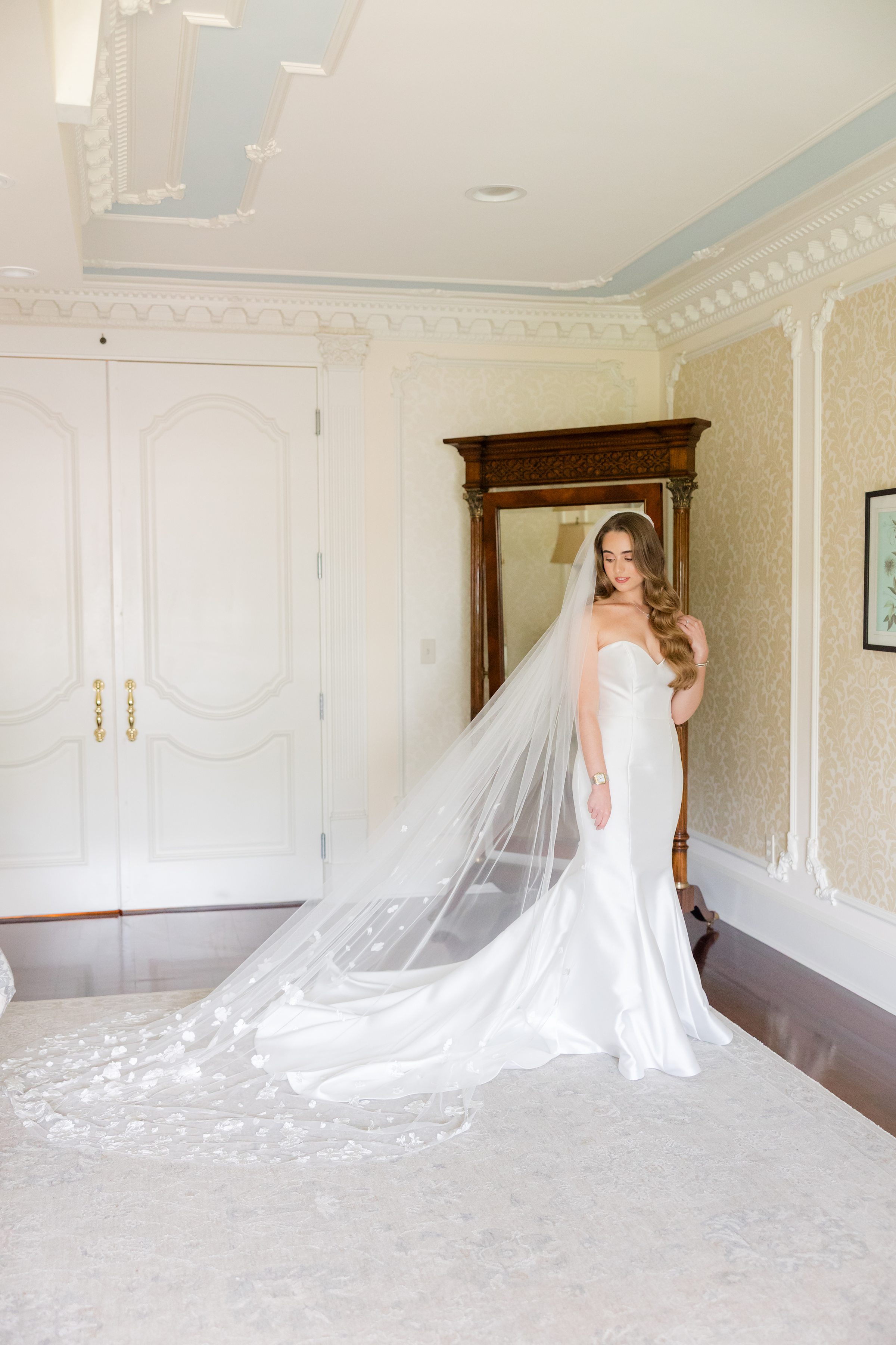 Full-body photo of bride looking to the side, wearing a mermaid-style dress and a long veil